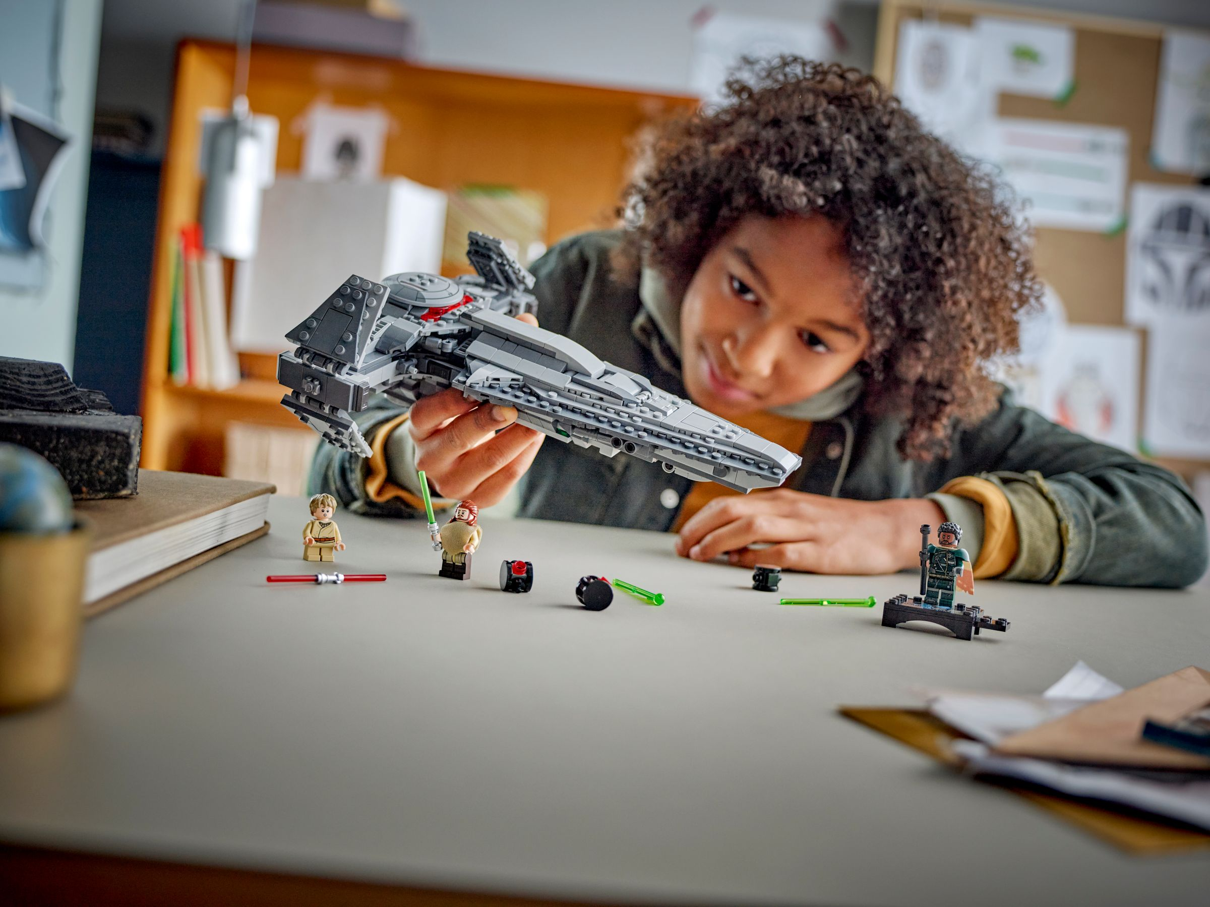 Ein Kind hält ein LEGO Star Wars Schiff. Minifiguren und Zubehör liegen auf dem Tisch. Das Kind lächelt.