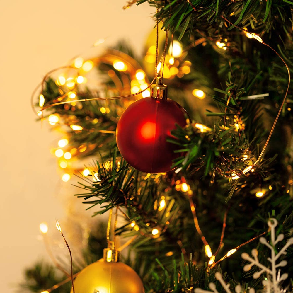 Nahaufnahme eines Weihnachtsbaums mit rotem Schmuck und Lichterketten. Ein goldener Schmuck und Schneeflocken sind ebenfalls sichtbar.