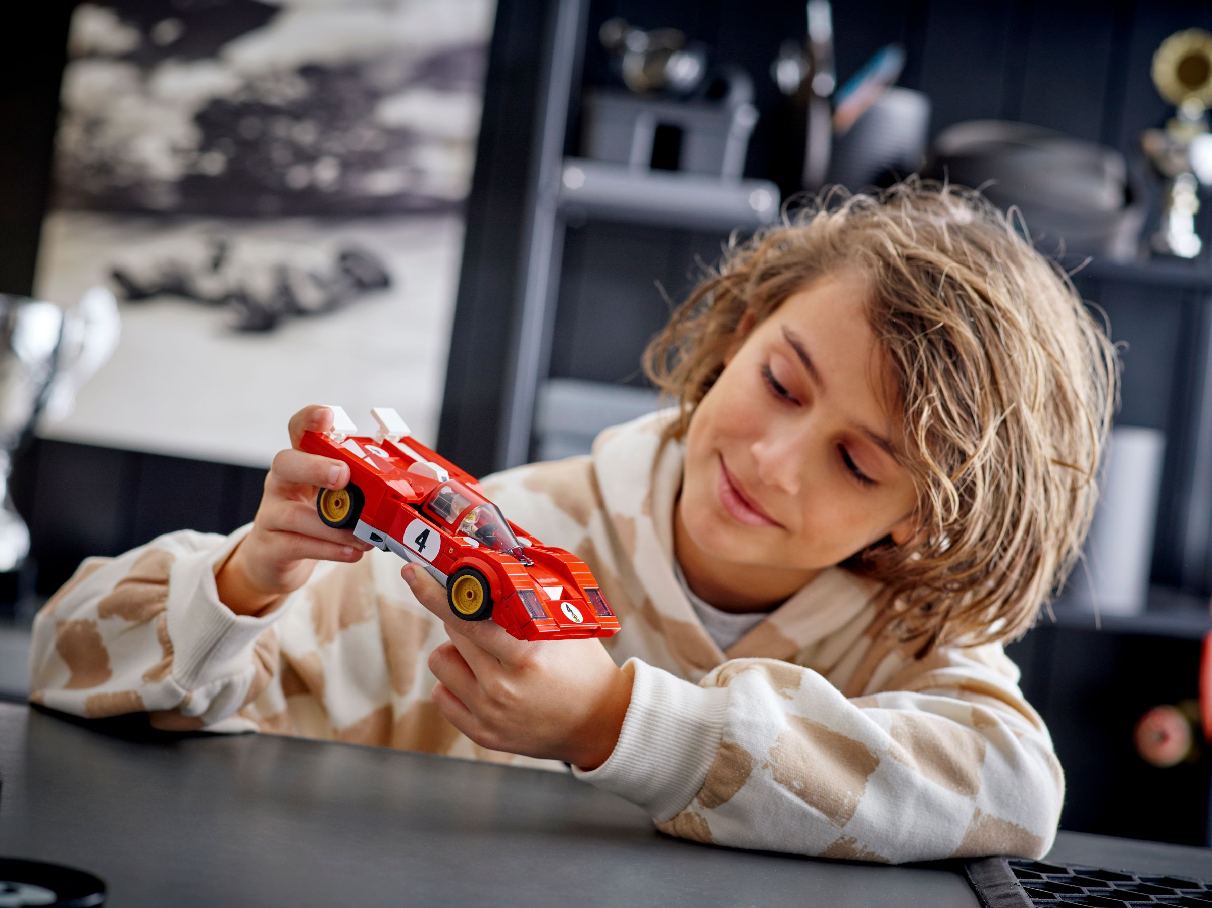 Ein Kind hält ein rotes Spielzeug-Rennauto mit weißem Streifen. Das Auto hat die Nummer 4.
