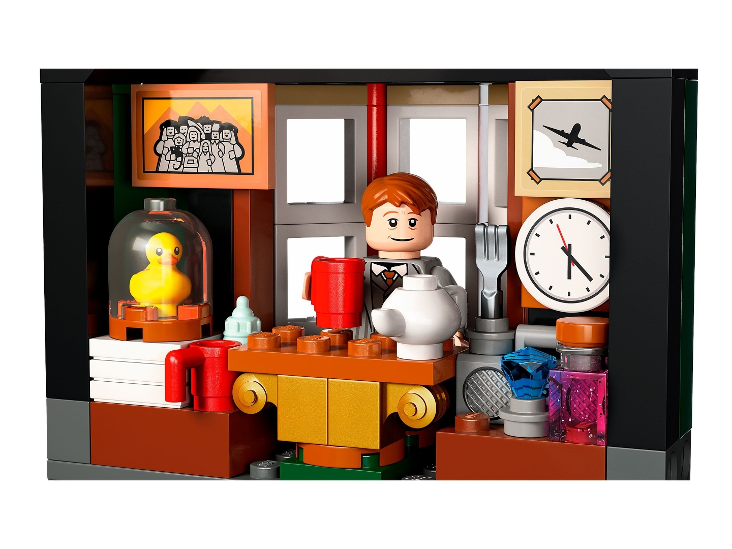Lego-Szene mit einer Figur, die einen roten Becher hält. Eine gelbe Ente in einem Glaskasten, eine Uhr und ein Flugzeugbild sind sichtbar.