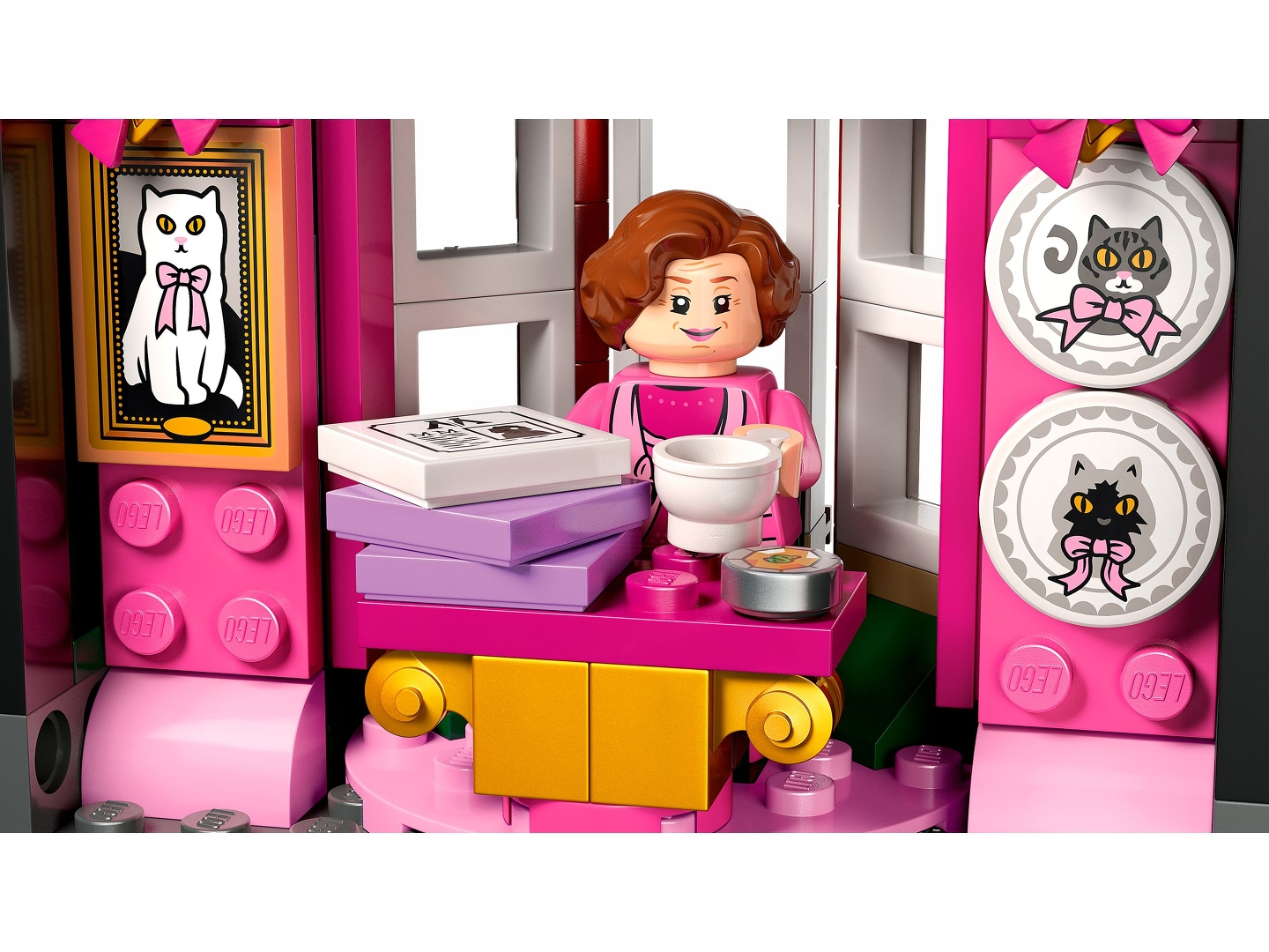 Lego-Szene mit einer Figur, rosa und goldenen Möbeln, Katzenbildern und einem Buch. Eine weiße Tasse, Katzenfutter und ein weißes Katzenbild.