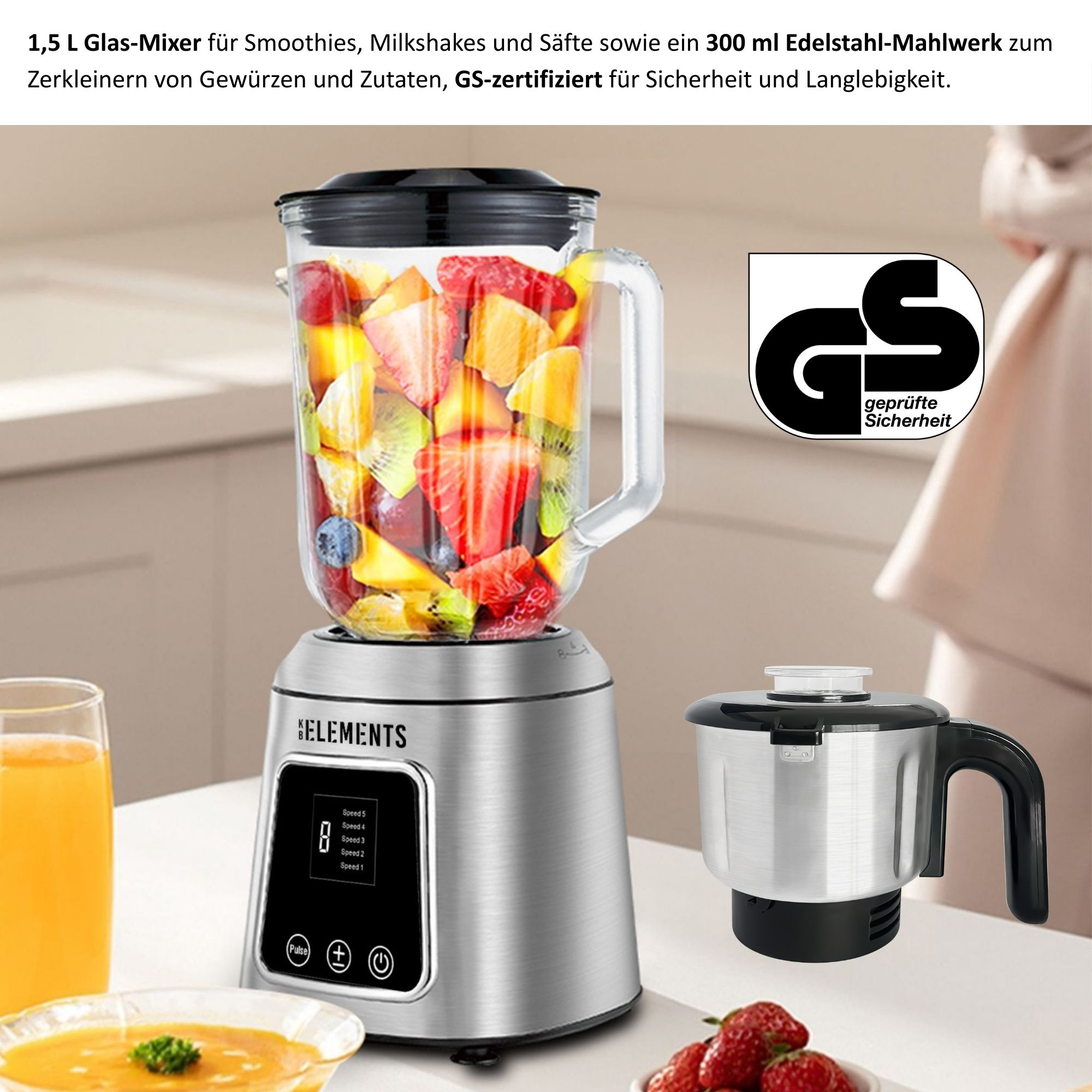 Mixer mit Früchten, kleinem Mahlwerk, Saftglas und Suppenschüssel. Erdbeeren im Vordergrund.