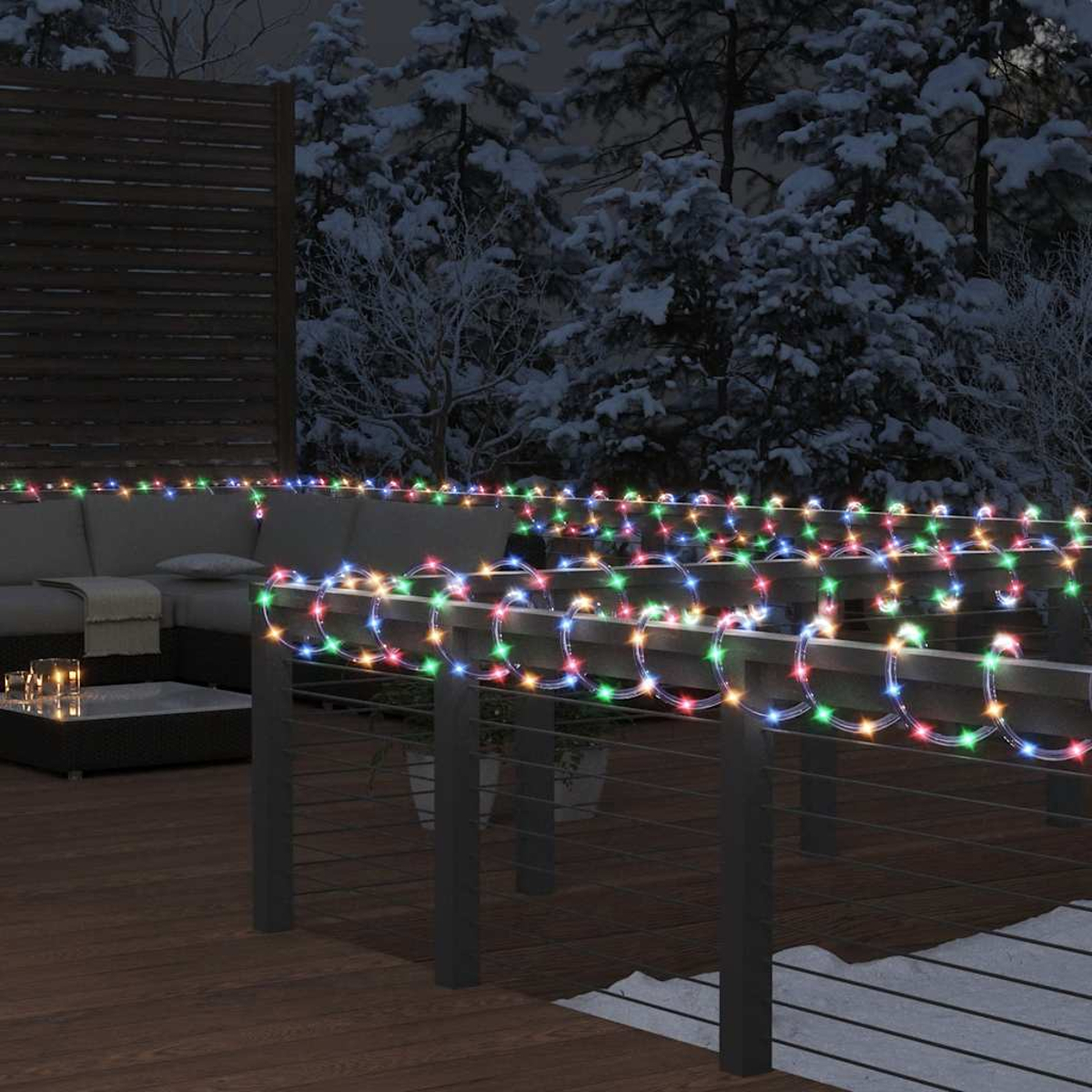 Eine nächtliche Szene im Freien mit einer Terrasse, bunten Lichtern, einem Sofa und schneebedeckten Bäumen im Hintergrund.