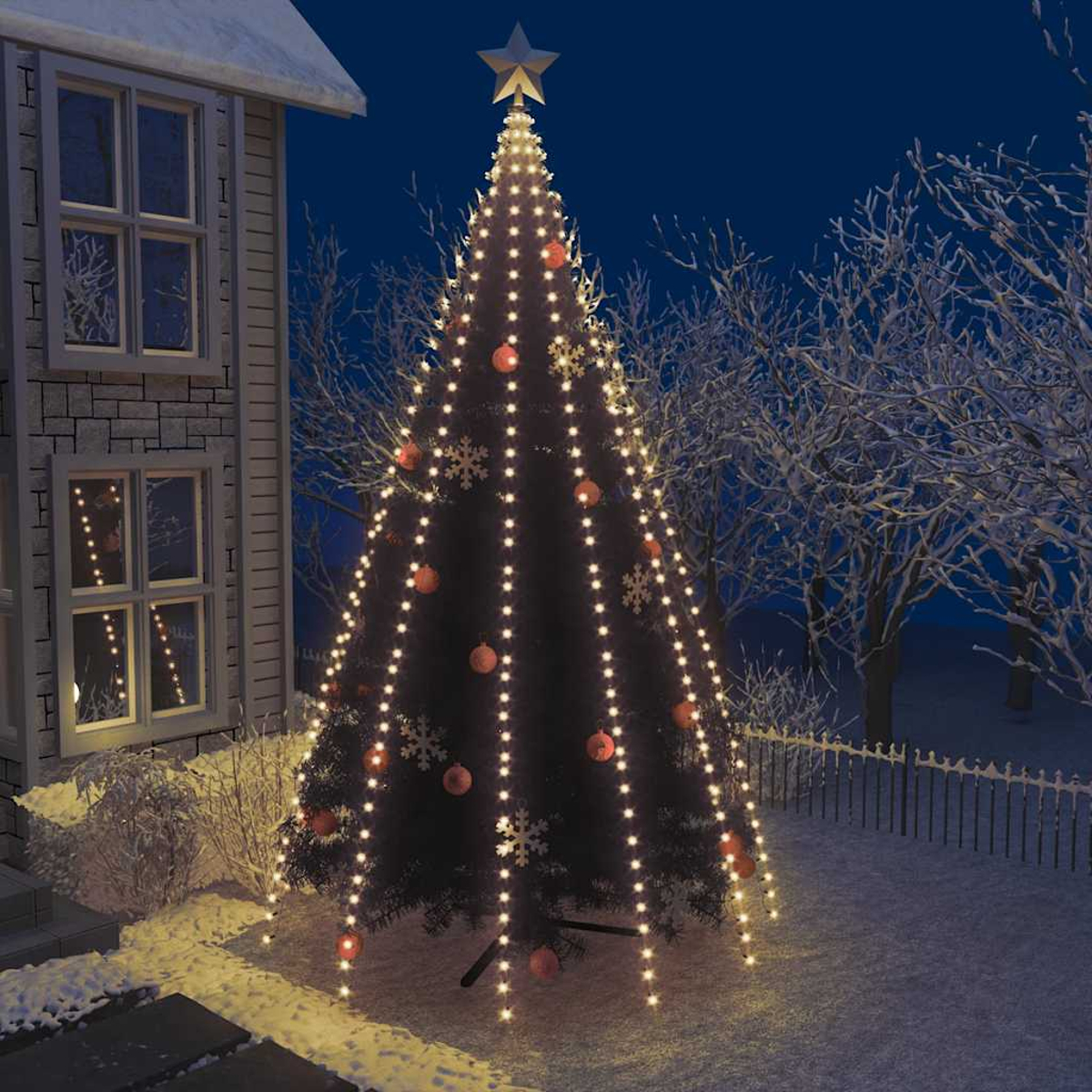 Ein geschmückter Weihnachtsbaum mit Lichtern und Ornamenten steht nachts vor einem Haus. Schnee bedeckt den Boden und die Bäume.