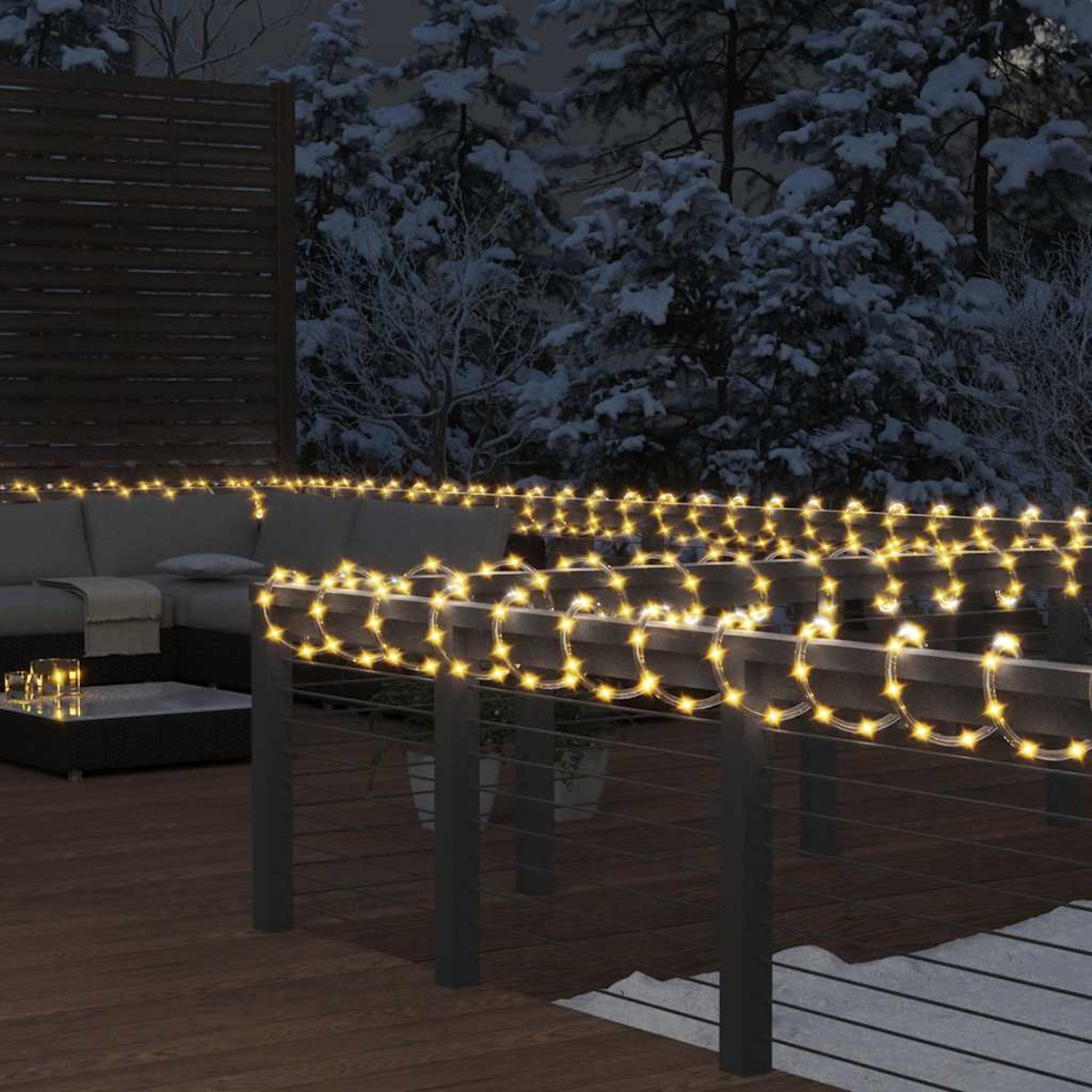 Außenszene bei Nacht, Lichterketten auf einem Geländer. Im Hintergrund ein Sofa und schneebedeckte Bäume. Das Deck ist aus Holz.