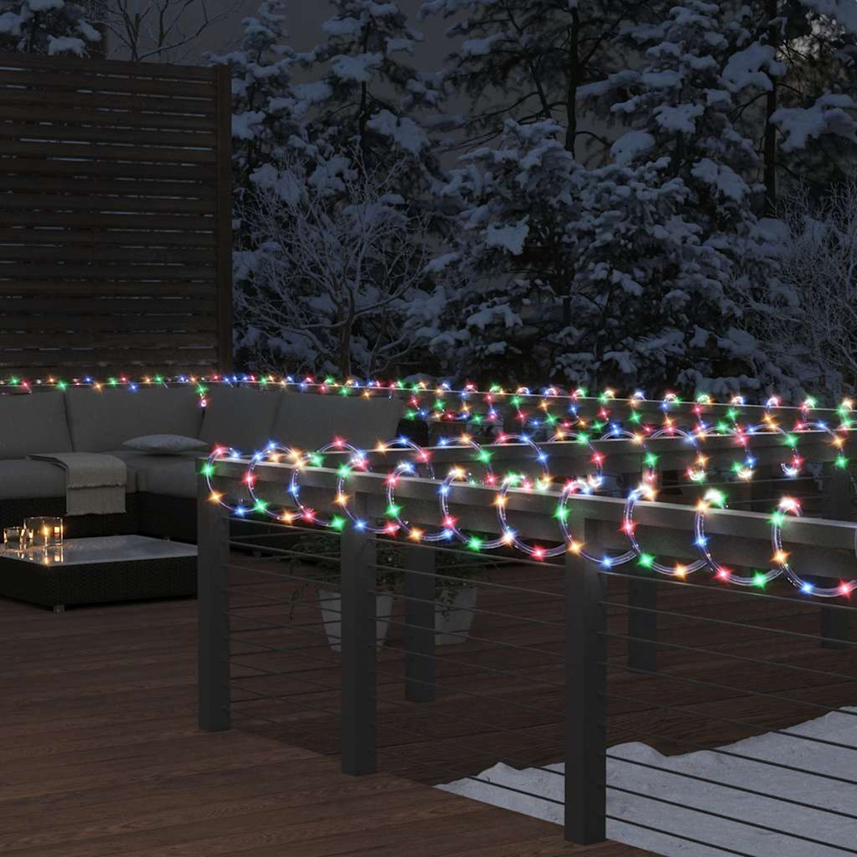Ein Deck mit bunten Lichterketten ist mit schneebedeckten Bäumen im Hintergrund dekoriert. Ein Sofa und ein Couchtisch sind sichtbar.