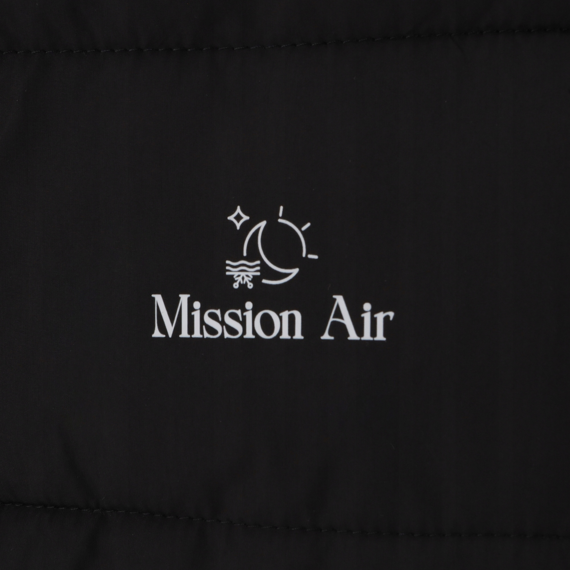 Czarna tkanina z białym tekstem i logo: 'Mission Air'. Logo zawiera księżyc, słońce, gwiazdę i symbol wody.