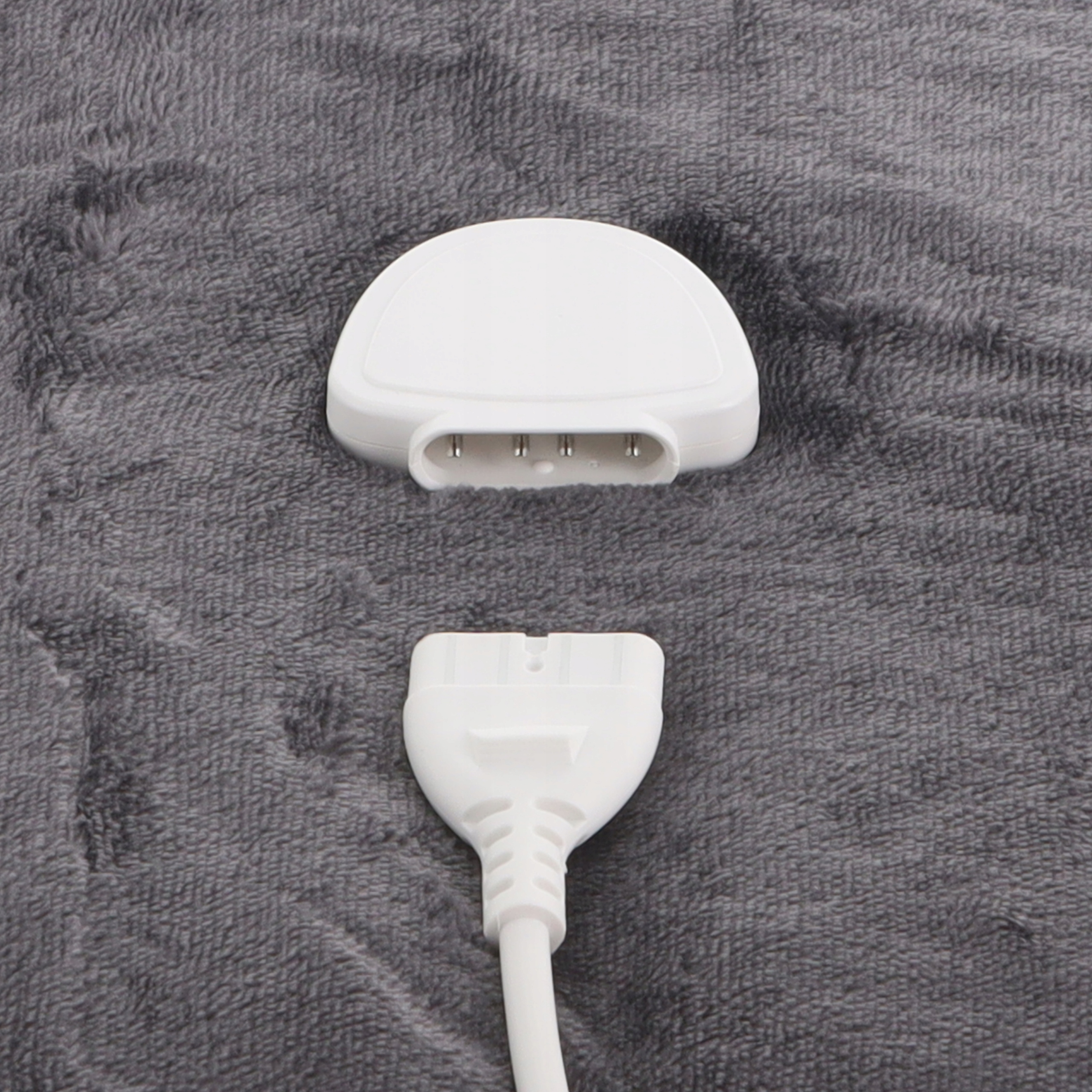 Białe elementy przewodu zasilającego na szarej, teksturowanej powierzchni. Jeden z pinami, drugi z wtyczką.