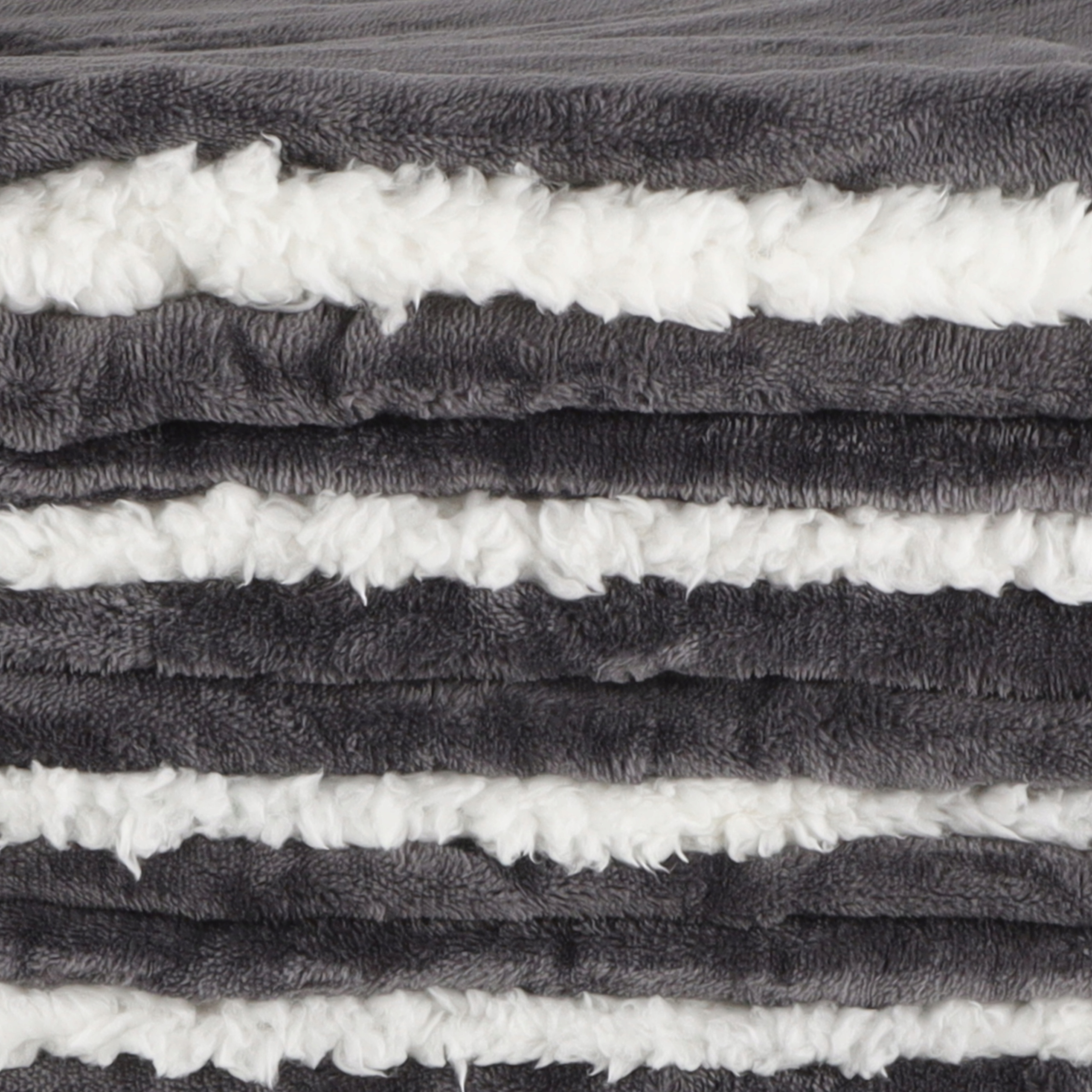 Zbliżenie na koc z naprzemiennymi szarymi i białymi puszystymi paskami. Tekstura wygląda na miękką i przytulną.