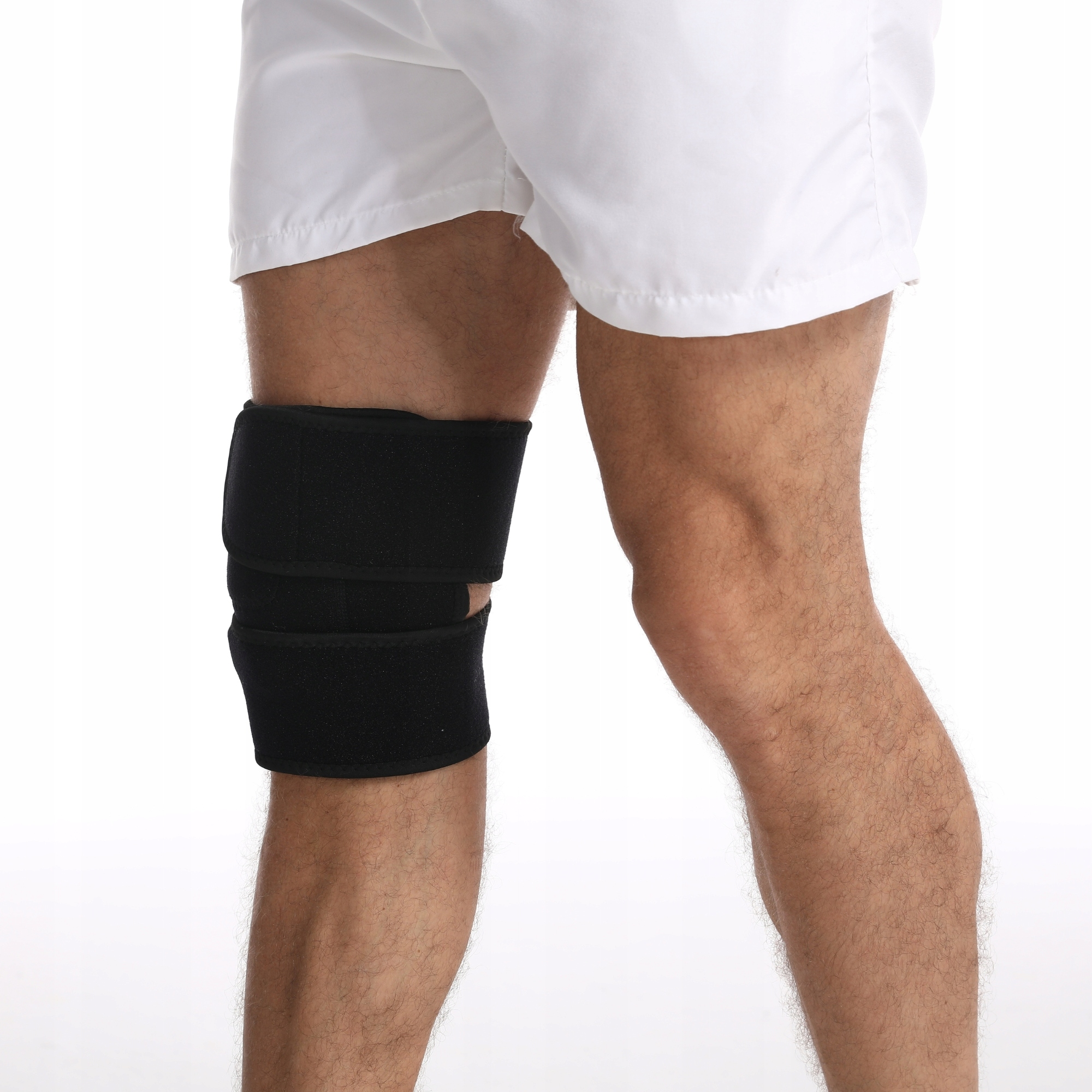 Noga osoby z czarnym ochraniaczem na kolano. Osoba ma na sobie białe szorty. Tło jest białe.