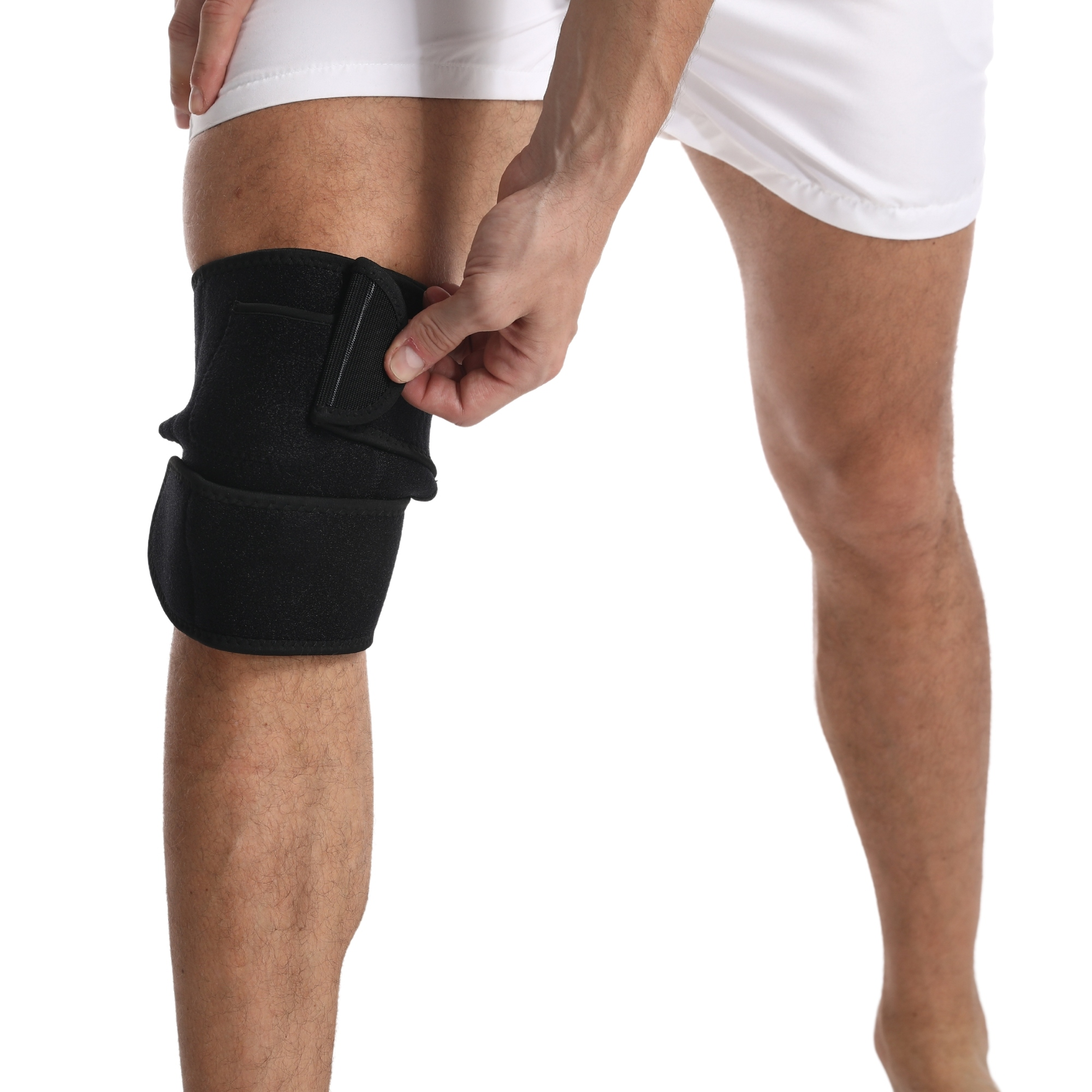 Osoba zakłada czarną ortezę kolana. Osoba ma na sobie białe szorty. Tło jest białe.