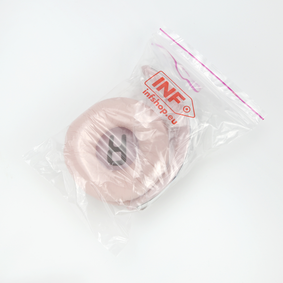 Różowa poduszka na ucho jest w przezroczystej plastikowej torbie z czerwonym logo INF. Torba leży na białym tle.