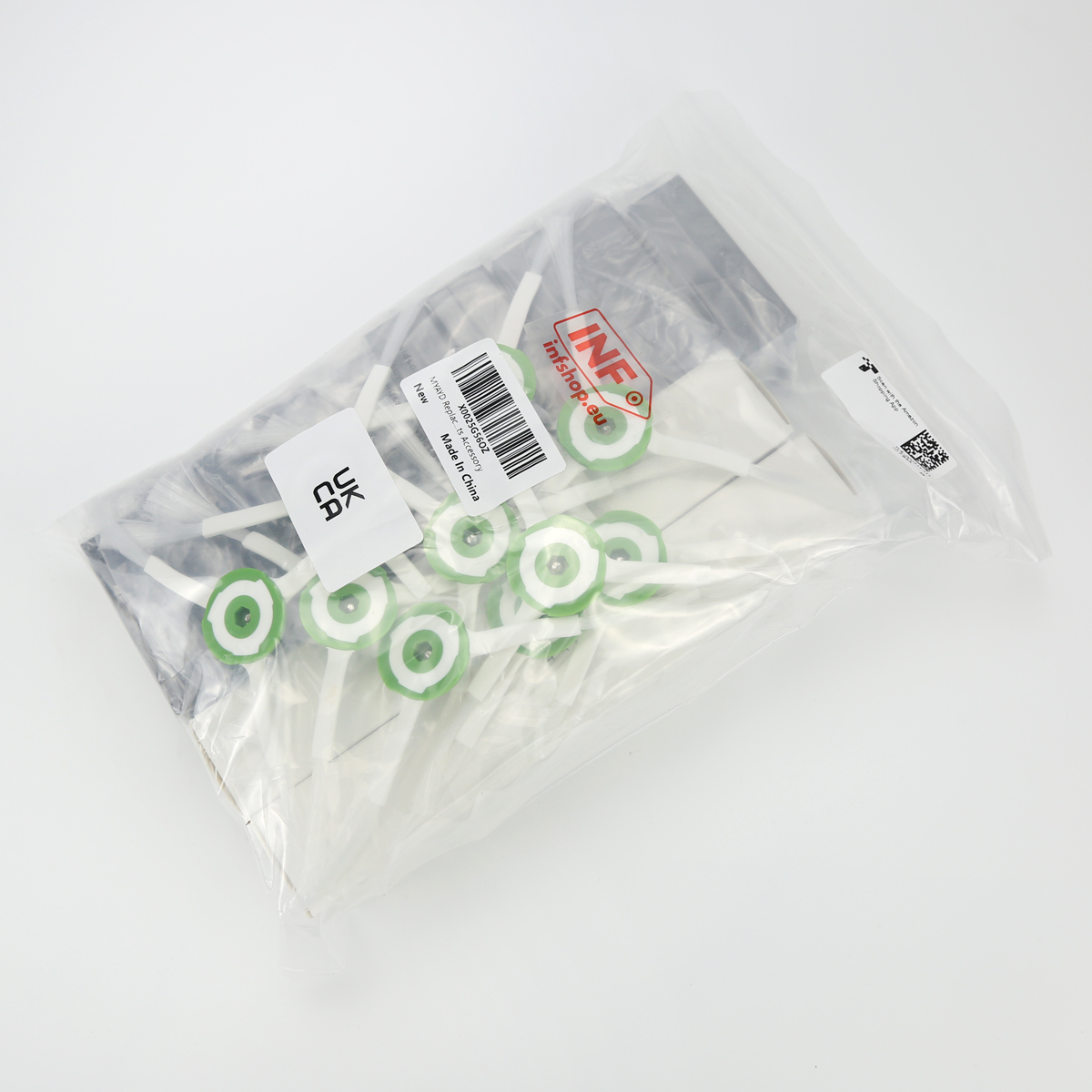 Przezroczysta plastikowa torba zawiera wiele białych i zielonych plastikowych części. Torba leży na białej powierzchni z kilkoma etykietami.