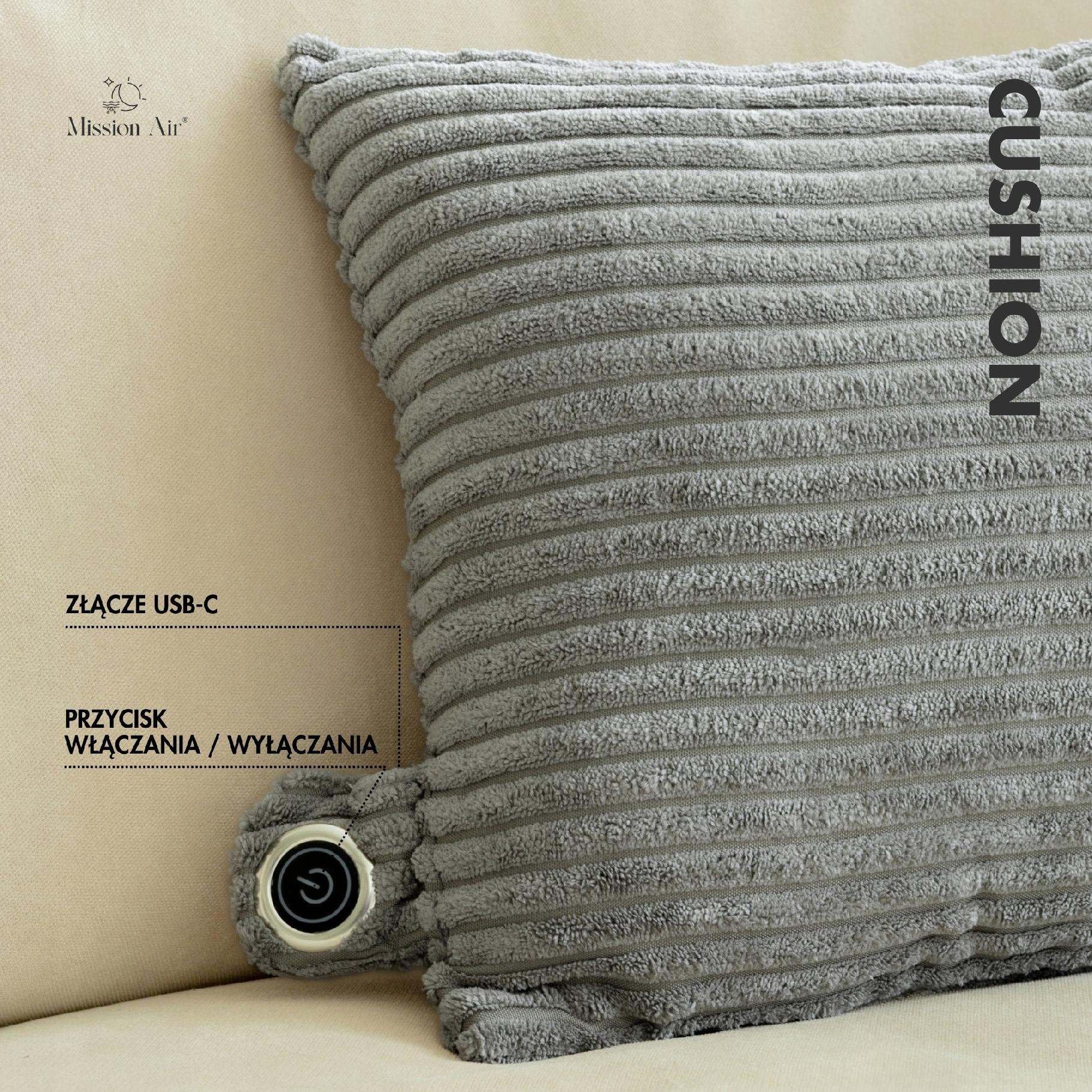 Szara, prążkowana poduszka z przyciskiem zasilania i portem USB-C, spoczywająca na beżowej powierzchni. Widoczny napis 'CUSHION'.