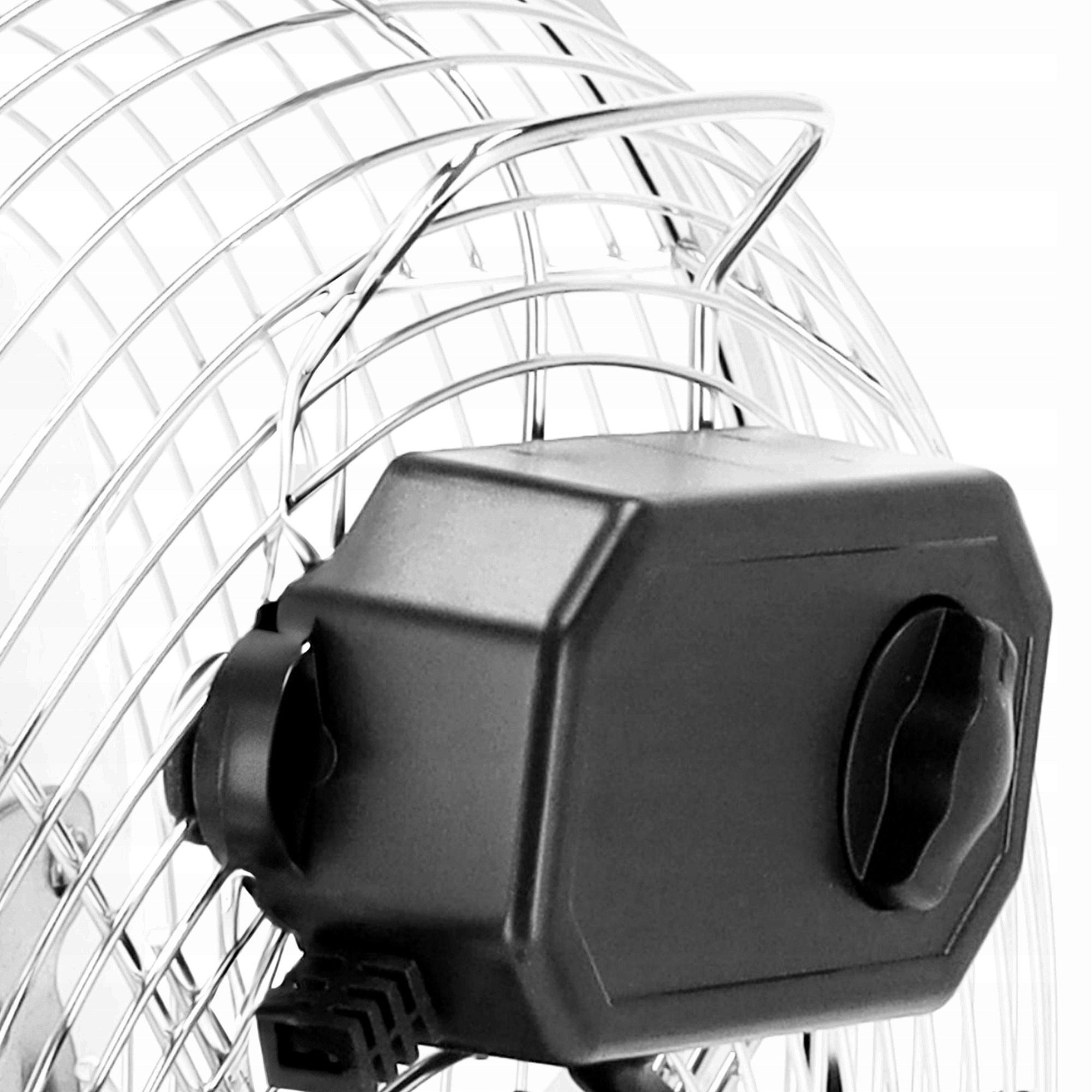 Zbliżenie czarnego silnika wentylatora z pokrętłami sterowania, na tle metalowej, okrągłej osłony wentylatora na białym tle.