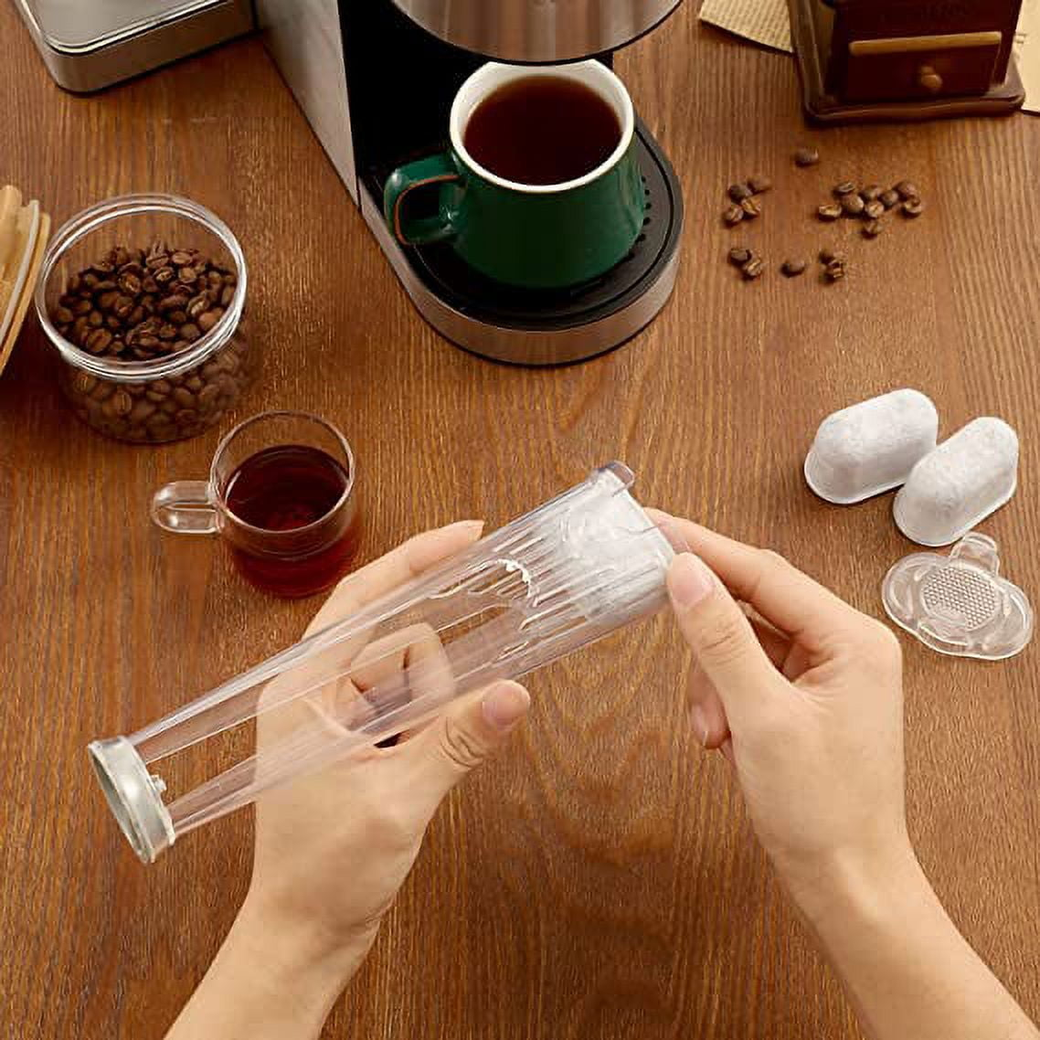 Hände halten einen durchsichtigen Filter. Kaffeemaschine, Kaffeetasse, Bohnen und Filter auf einem Holztisch.