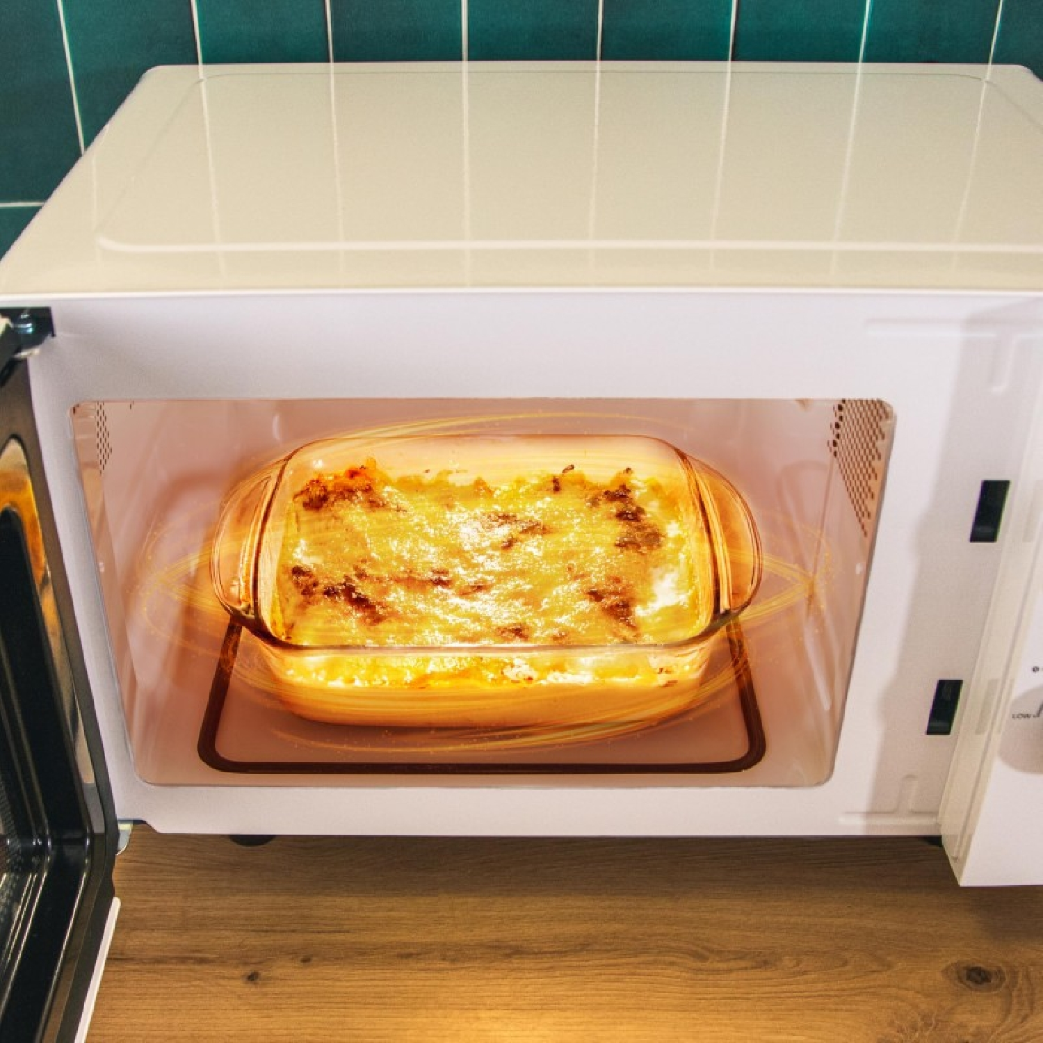 Una pirofila all'interno di un microonde. Il piatto è pieno di cibo e si illumina. Lo sportello del microonde è aperto.