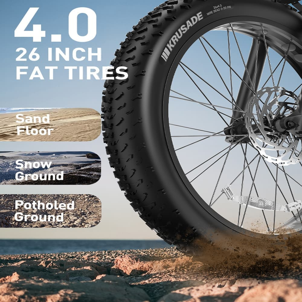 Primer plano de una rueda de bicicleta de neumáticos anchos en la playa. El texto muestra '4.0 26 pulgadas neumáticos anchos'. Demuestra uso en arena, nieve y terreno irregular.