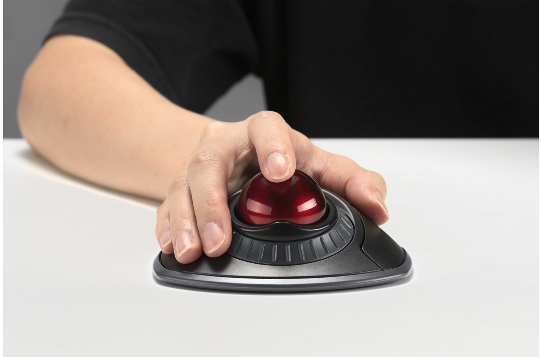Una mano usa un mouse trackball. La sfera è rossa, il mouse nero e lo sfondo sfocato.