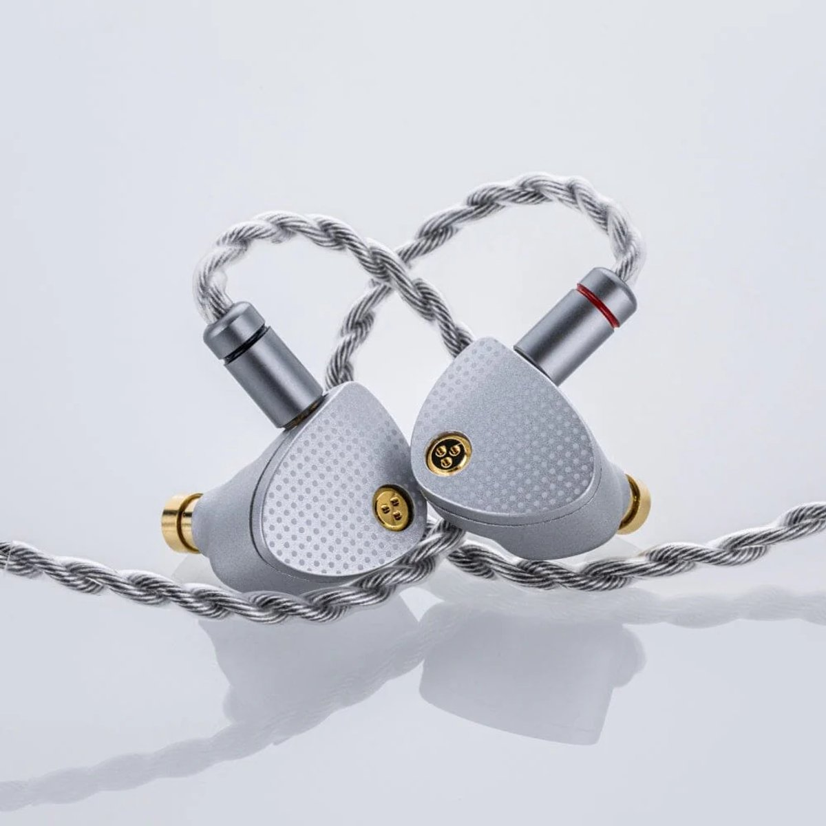 Twee zilveren in-ear-hoofdtelefoons met een gevlochten zilveren kabel. Elke oortelefoon heeft een gouden mondstuk en een getextureerd oppervlak.