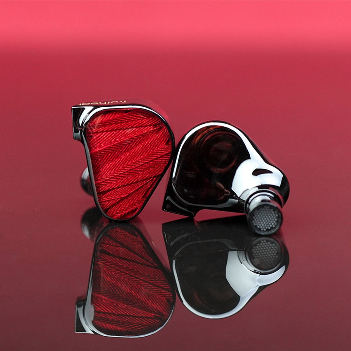 Zwei schwarze und rote In-Ear-Kopfhörer auf einer reflektierenden Oberfläche, vor rotem Hintergrund. Ein Kopfhörer ist abgewinkelt.