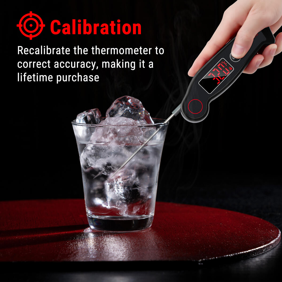 A hand holds a thermometer in ice water. The thermometer reads 32.0. The scene is on a dark red surface with black background.