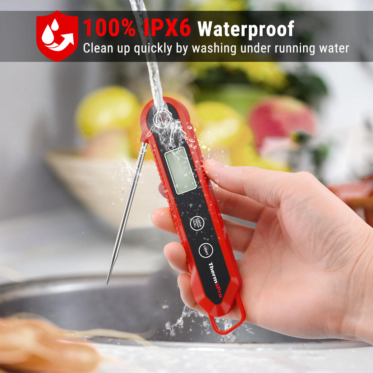 A red digital thermometer is washed with water. The screen is on. The thermometer is held by a hand. The background is blurry.