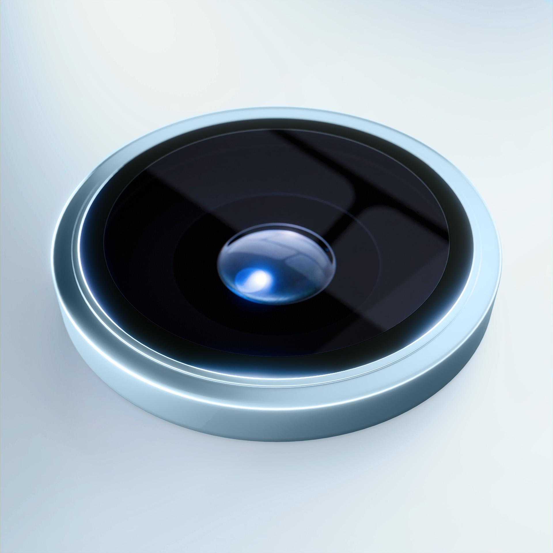 Primo piano di un obiettivo fotografico con centro nero riflettente, circondato da un anello azzurro chiaro, su sfondo bianco.