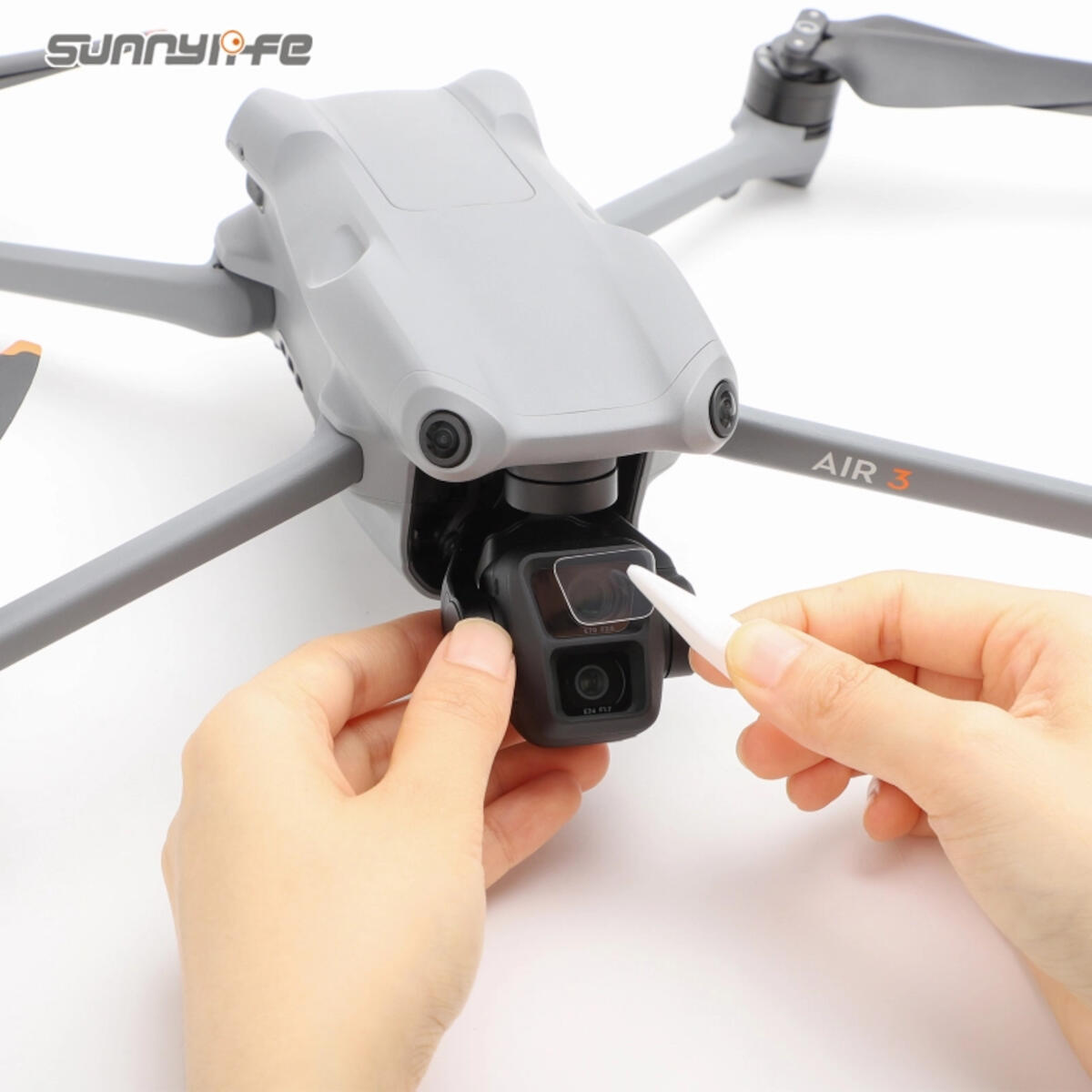 Een grijze drone met handen die de cameralens schoonmaken. Op de drone staat 'AIR 3'. Het logo 'sunny life' is zichtbaar.