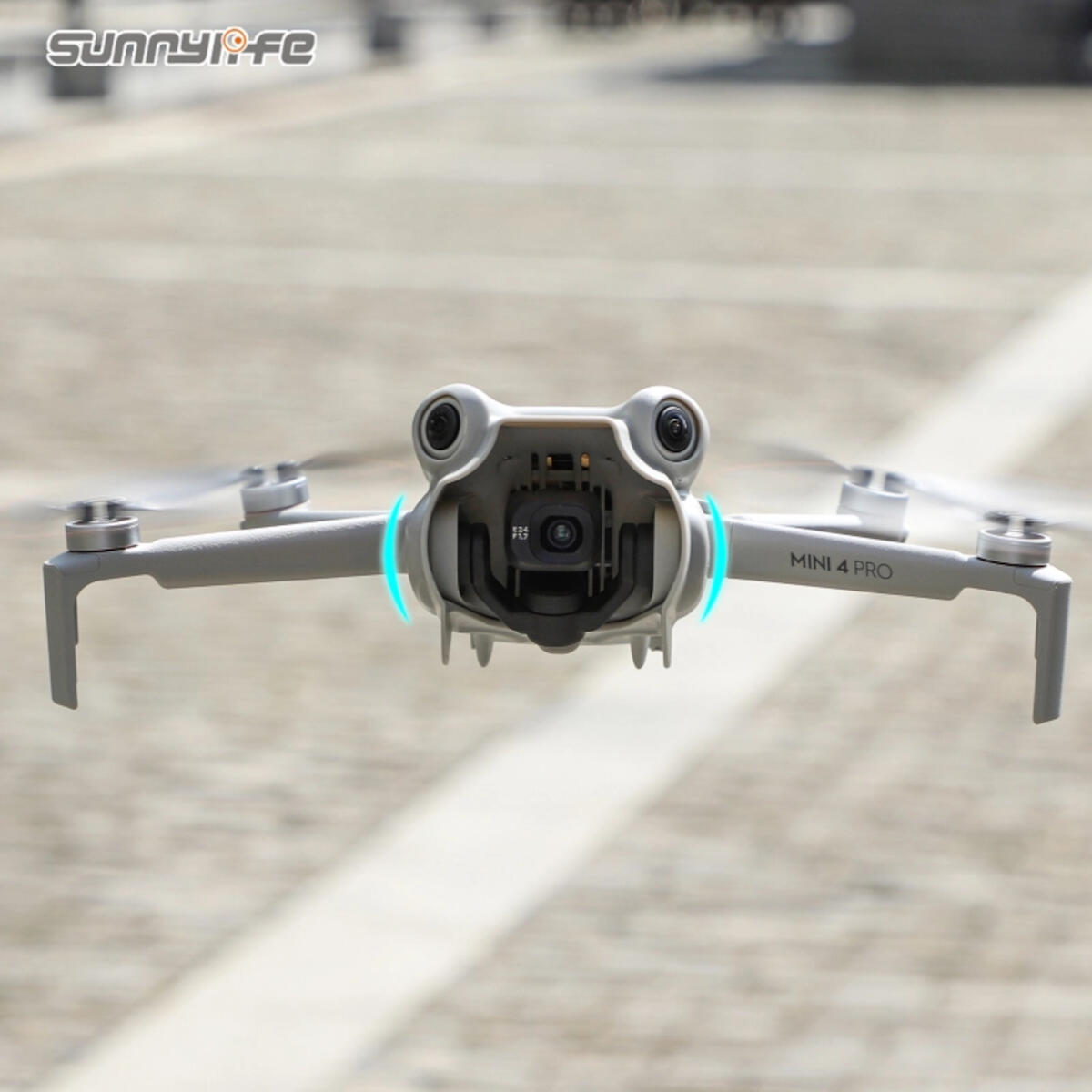 A gray Mini 4 Pro drone in mid-air, camera facing forward. The background is a blurred gray surface.