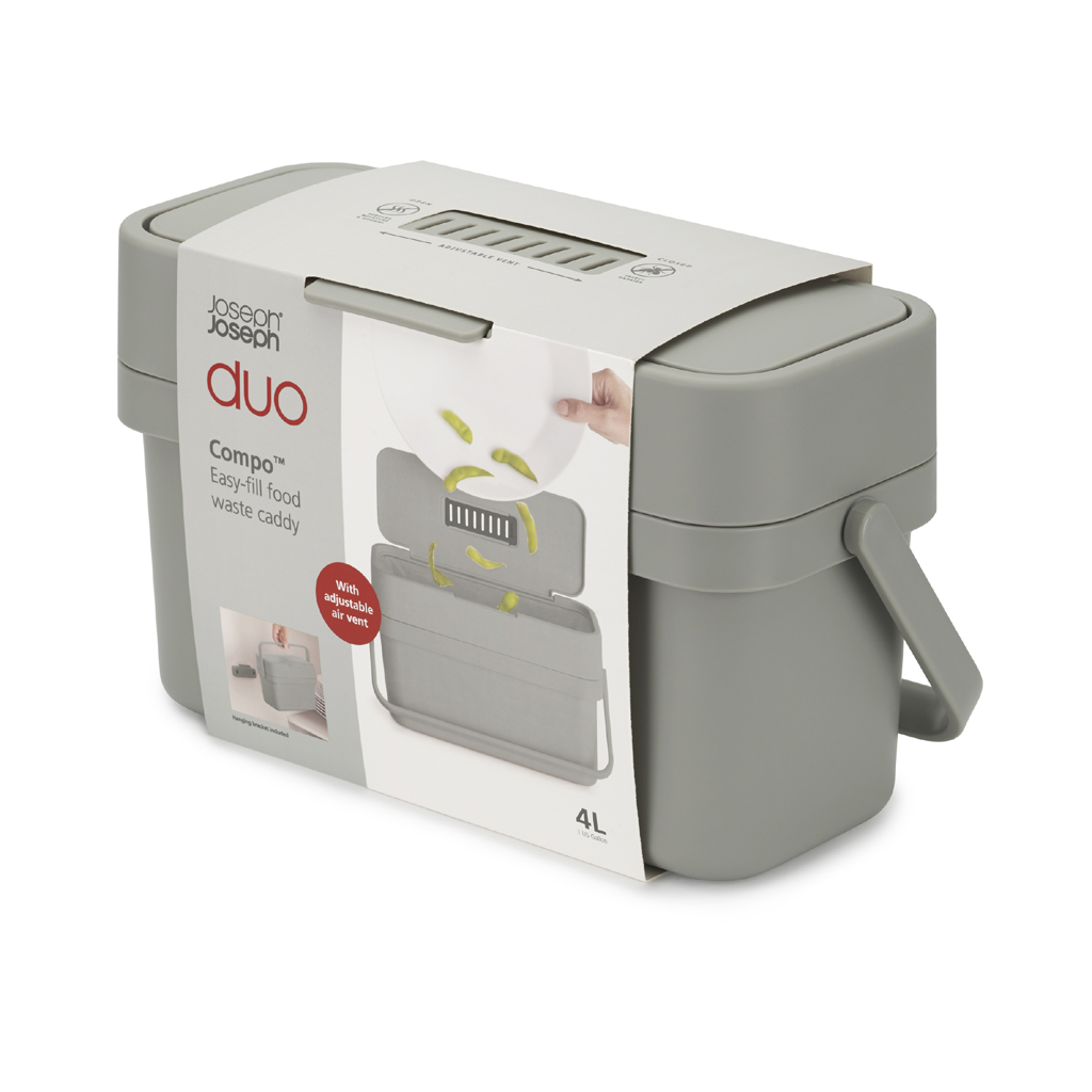 Un cubo de basura para alimentos gris Joseph Joseph Duo Compo. Tiene un asa y está en su embalaje. El embalaje muestra comida que se está añadiendo.