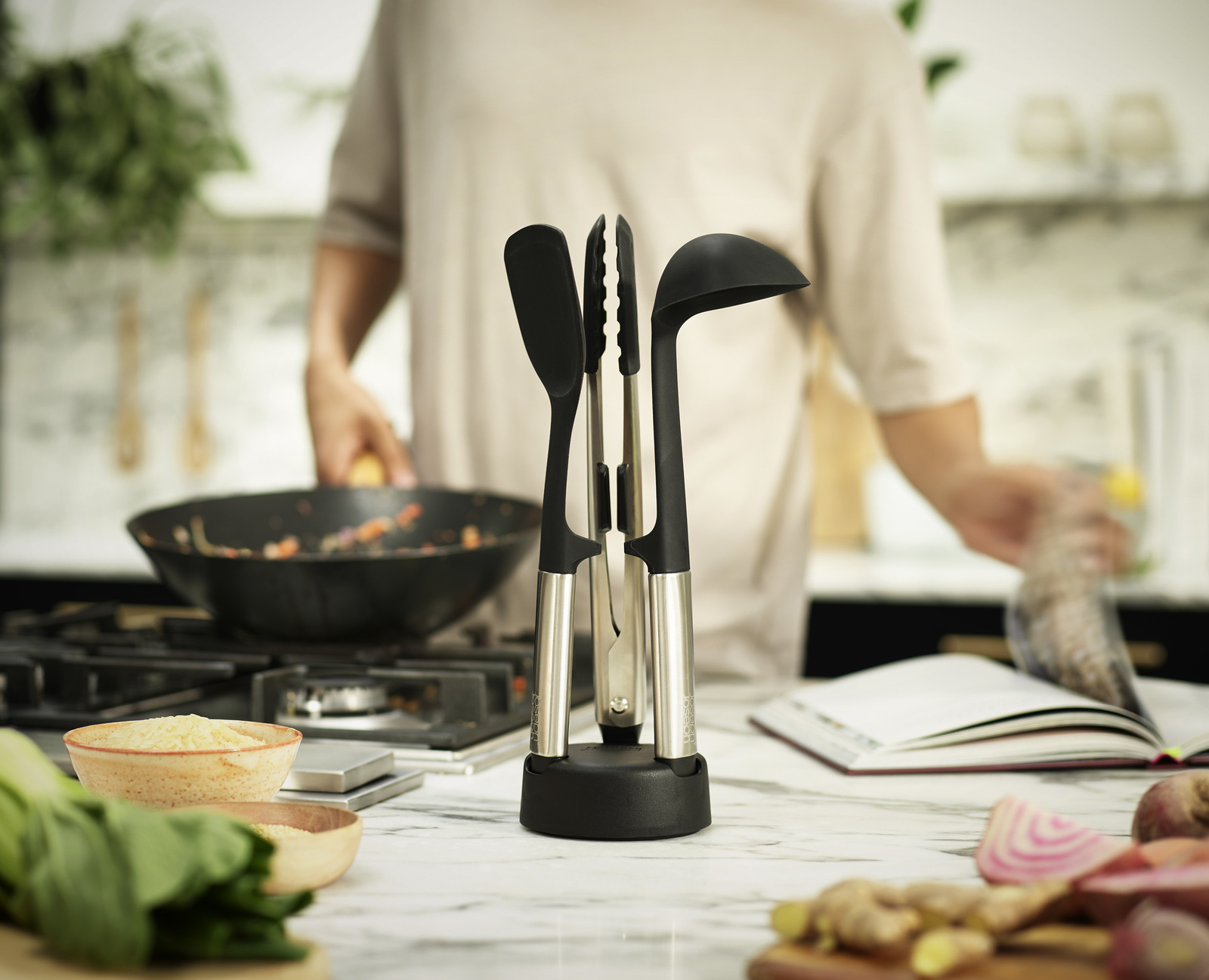 Una persona cocina en una cocina. Utensilios de cocina en primer plano. Una sartén con comida en la estufa. Hay cuencos de comida.