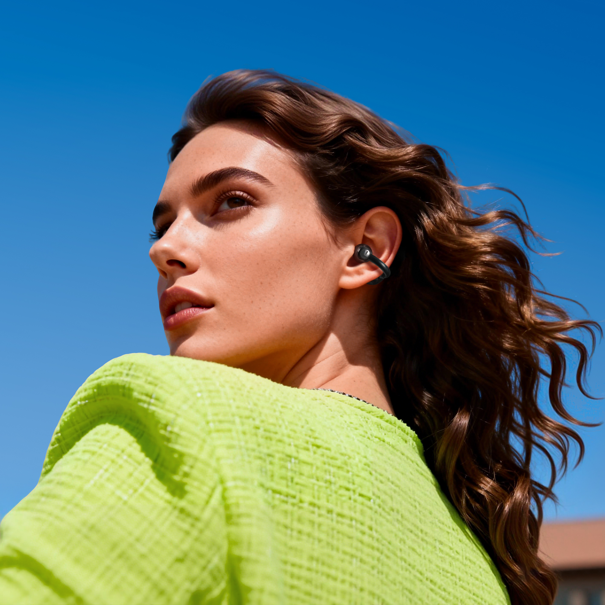 Donna con auricolari, top verde, guarda altrove. Capelli castani contro cielo blu.