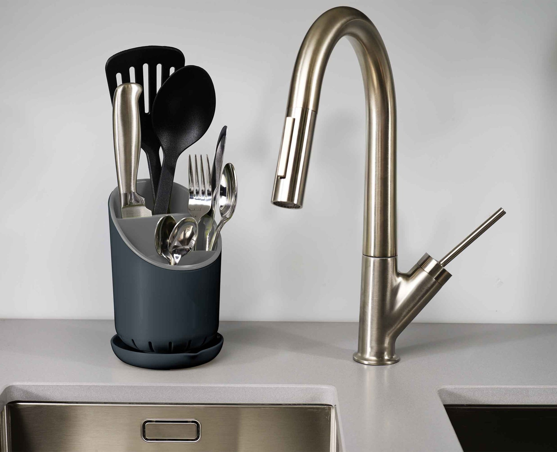 Escena de cocina con grifo, utensilios en un soporte y fregadero. Los utensilios incluyen cuchillo, cuchara y espátula ranurada.
