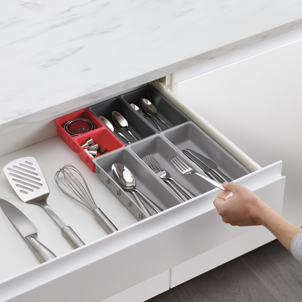 Un cajón abierto muestra cubiertos y utensilios de cocina organizados. Los utensilios incluyen cucharas, tenedores, cuchillos, espátula y batidor.