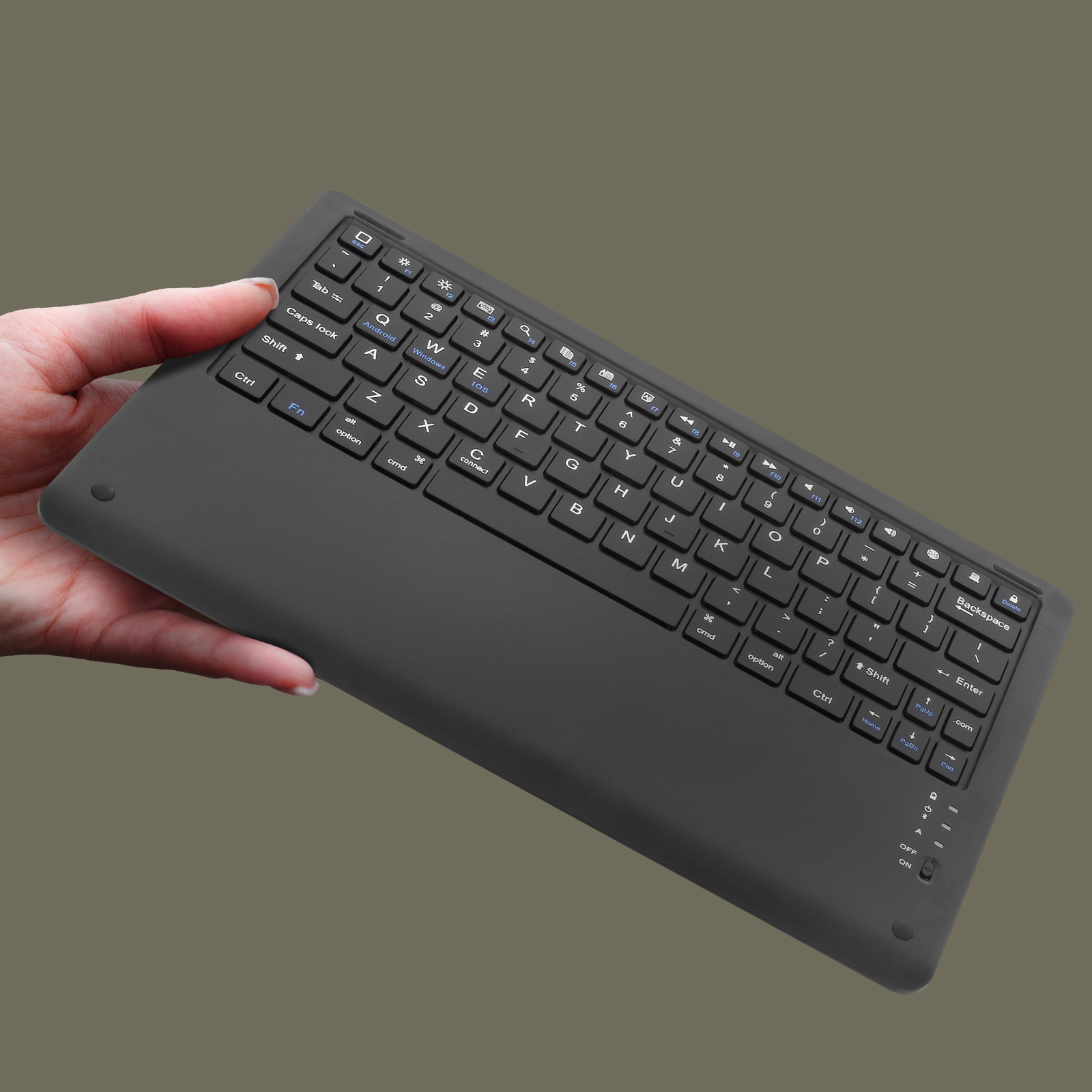 Eine Hand hält eine schwarze, kabellose Tastatur. Die Tastatur hat verschiedene Tasten und befindet sich auf braunem Hintergrund.
