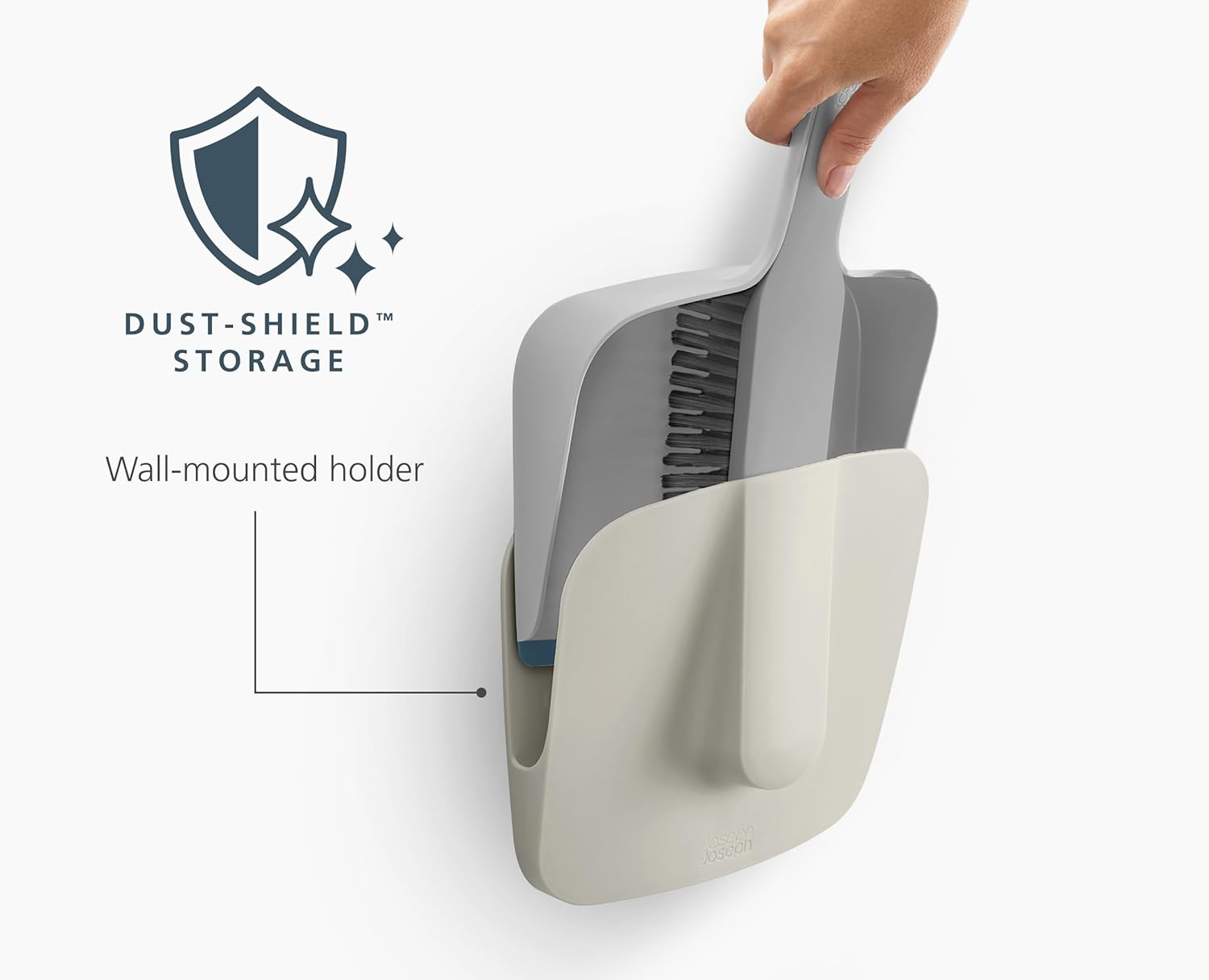 Una mano sostiene un recogedor y un cepillo grises en un soporte de pared. El soporte es beige. Logotipo y texto 'Dust-Shield Storage'.