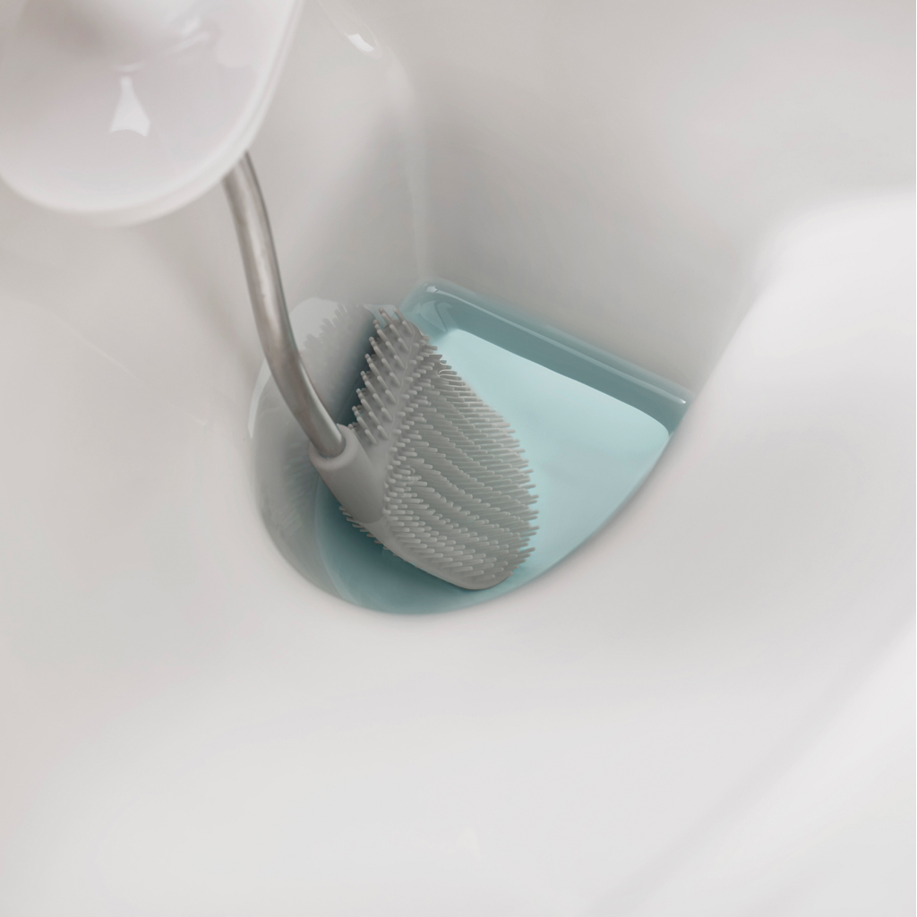 Un cepillo de inodoro gris con cabezal suave descansa en un soporte azul claro dentro de un inodoro blanco.