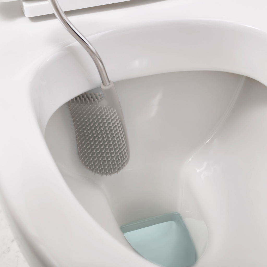 Primer plano de un inodoro blanco con un cepillo gris dentro. El cepillo tiene púas. El inodoro tiene una sección azul.
