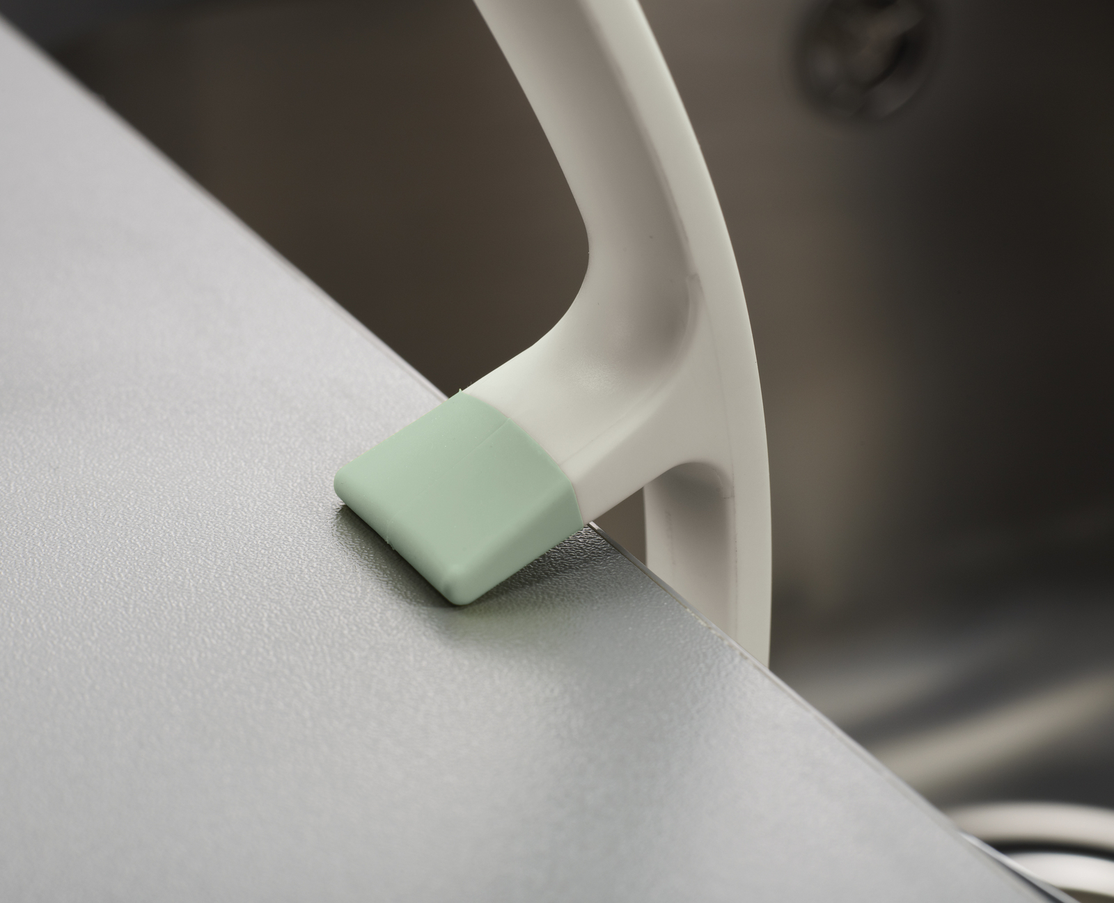 Vista de cerca de un mango blanco con una pieza final verde claro, posiblemente parte de un electrodoméstico de cocina, sobre una superficie brillante.