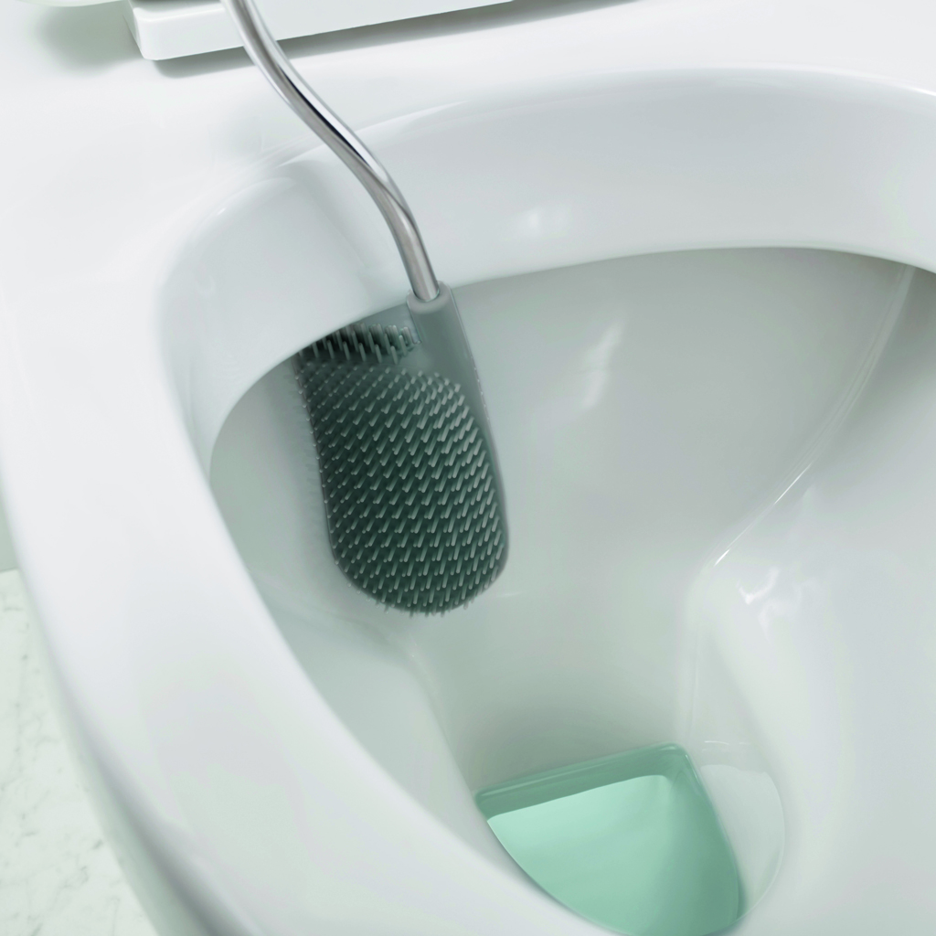 Un cepillo de inodoro está dentro de un inodoro blanco. El cepillo es gris con cerdas y el mango es plateado.