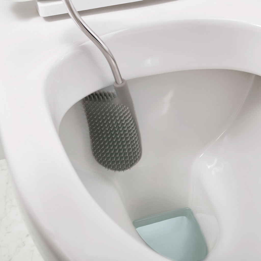 Un cepillo de inodoro gris está dentro de un inodoro blanco. La cabeza del cepillo tiene muchas cerdas pequeñas. Hay un elemento azul en la parte inferior.