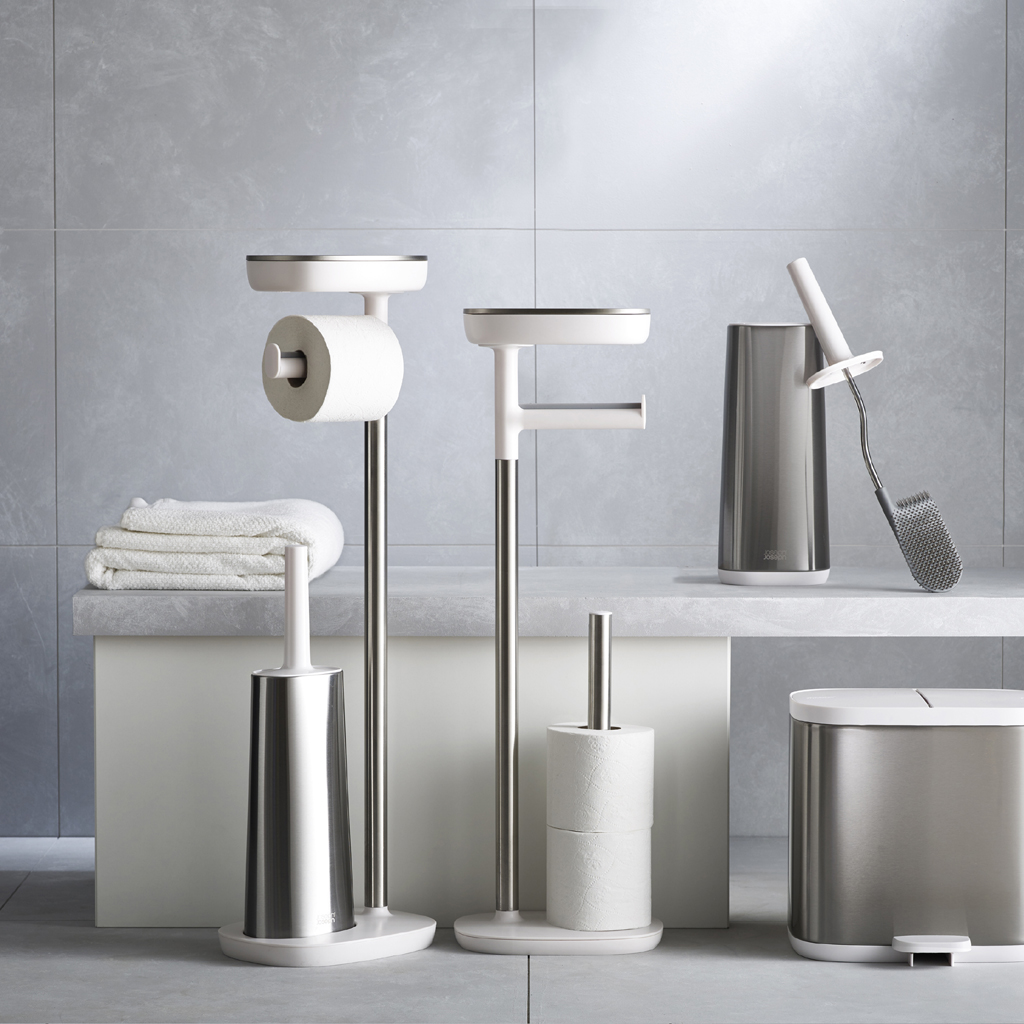 Juego de accesorios de baño: portarrollos, cepillo, papelera y toallero. Tonos blancos y plateados sobre fondo gris.
