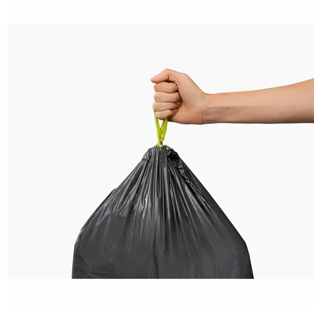 Una mano sostiene una bolsa de basura negra con una cinta verde sobre un fondo blanco.