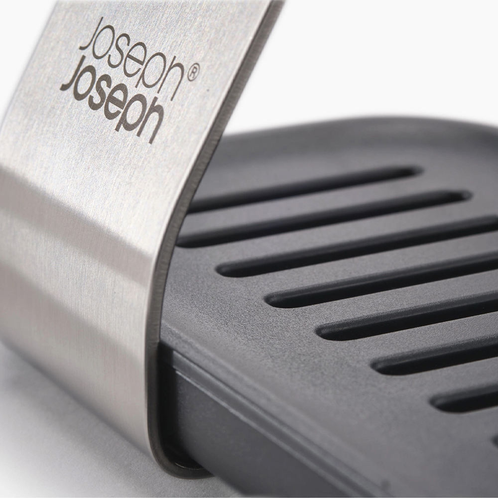 Primer plano de un portautensilios de cocina Joseph Joseph. Marco de metal plateado con la marca. Base ranurada negra.