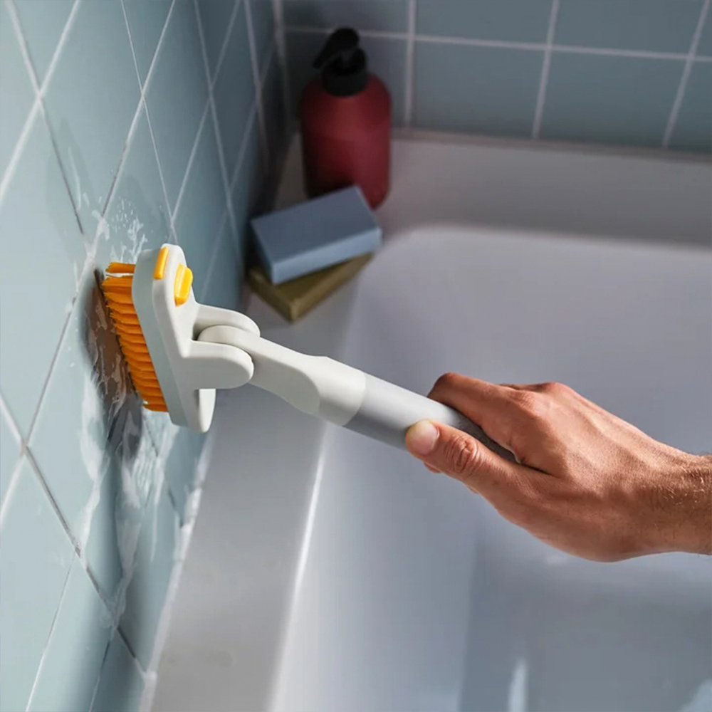 Una persona limpia una pared de azulejos azules con un cepillo. Hay una bañera, jabón y una botella en el fondo.