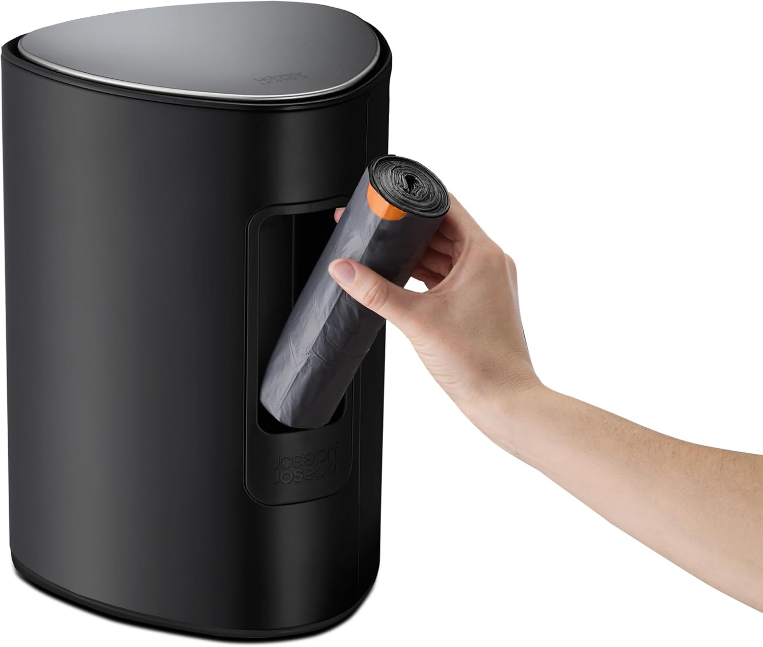 Una mano saca un rollo de bolsas de basura negras de un cubo de basura negro. El cubo tiene una tapa plateada.