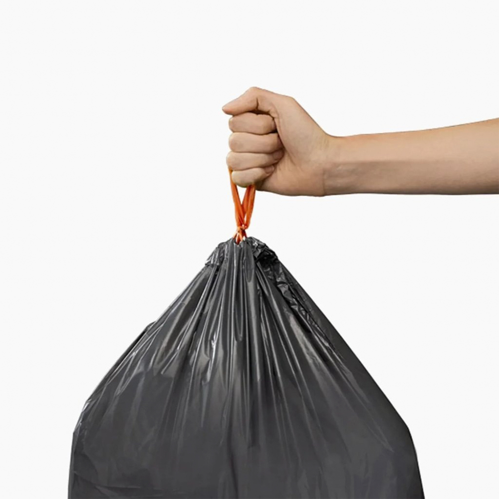 Una mano sostiene una bolsa de basura negra atada con naranja sobre un fondo blanco.