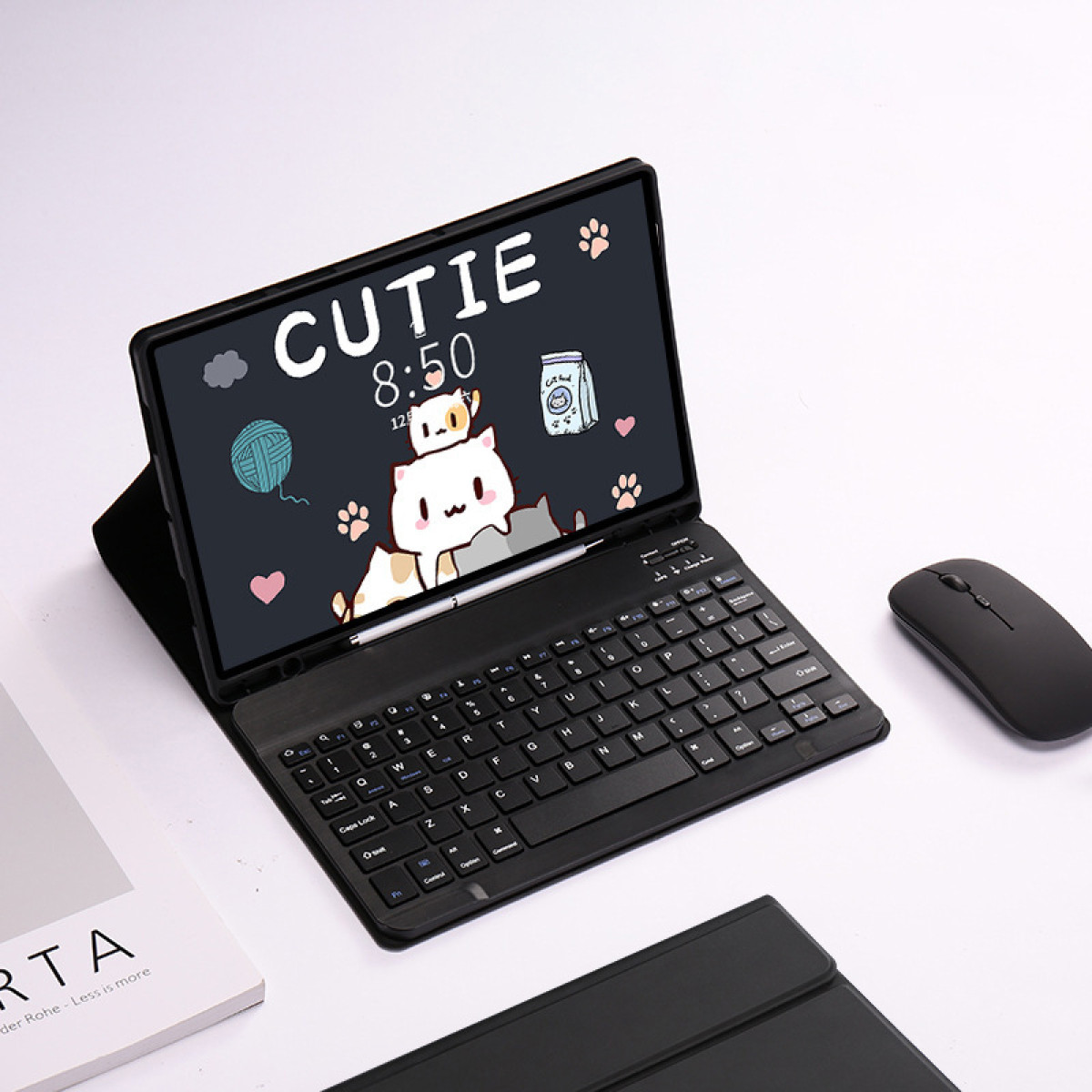 Tablet z klawiaturą i myszą leży na białej powierzchni. Tablet wyświetla ekran z motywem kota. Książka po lewej na dole.