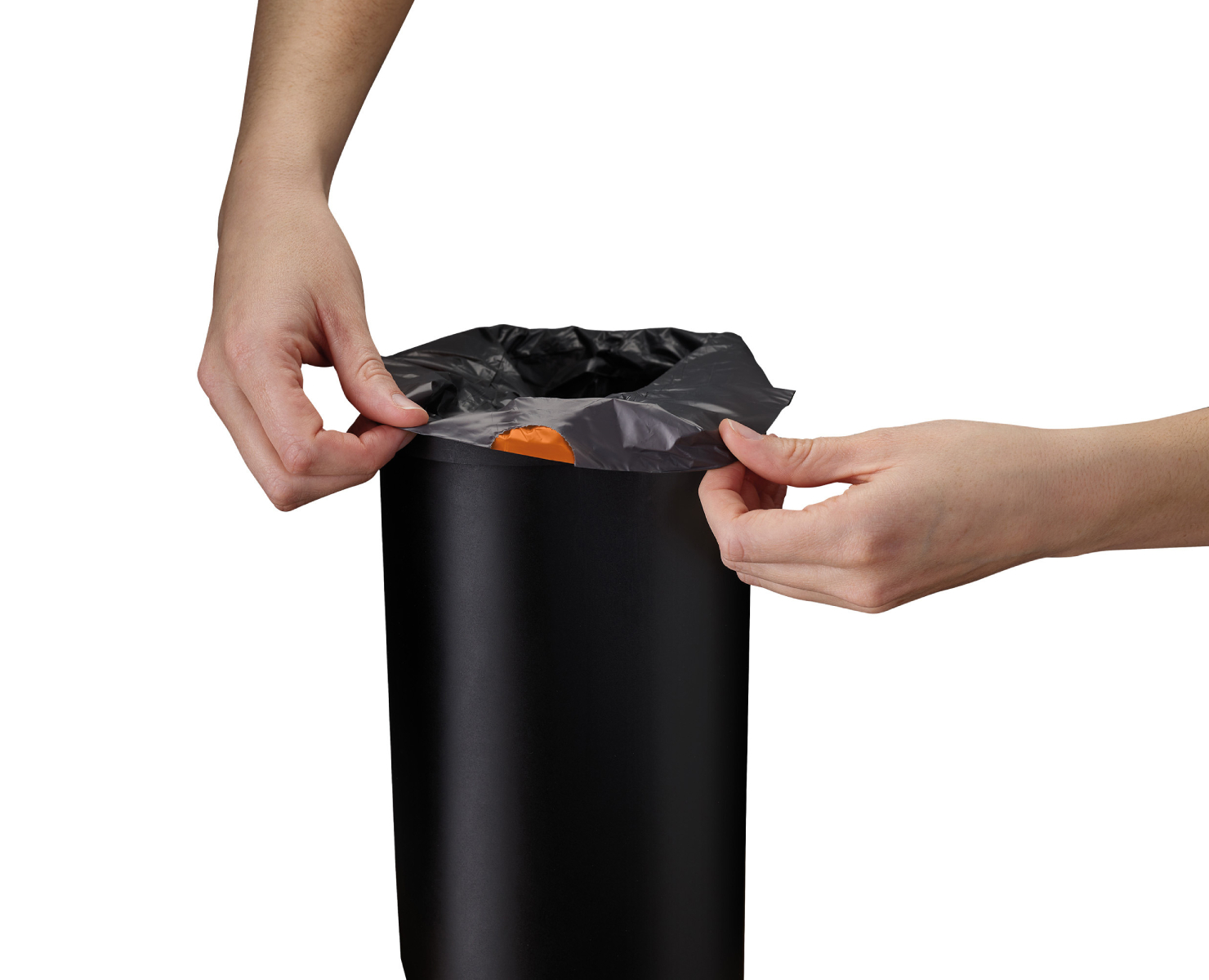 Manos abriendo una bolsa de basura negra de un cubo de basura negro. Un objeto naranja es visible dentro de la bolsa.